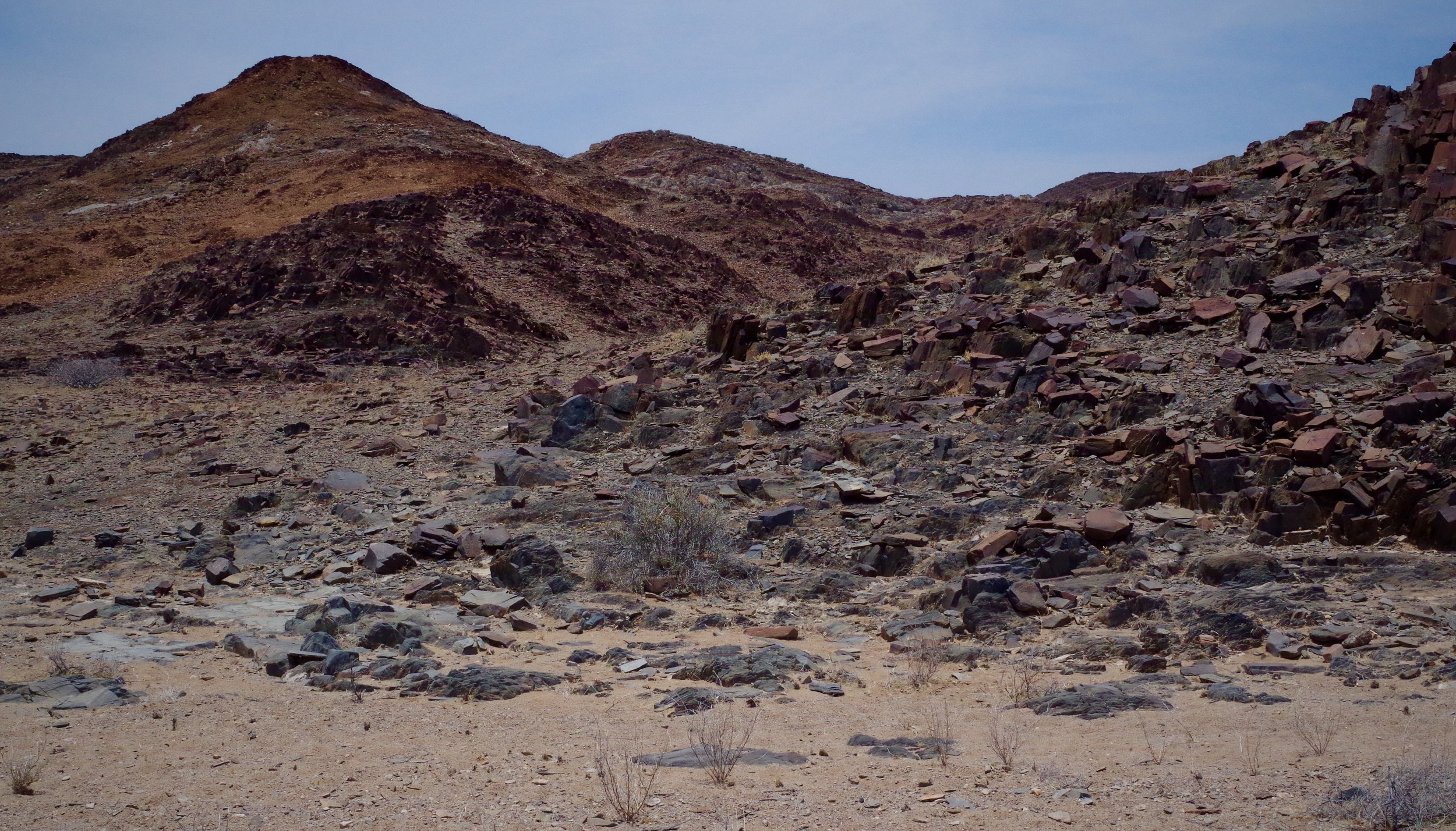 Desert Flint and Pebble Rocks polished by the result if wind and sand over millions of years lie in black heaps around rust-red mountains and hills.