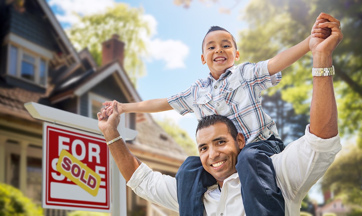 Family celebrating homeownership in front of a home with a sold sign.