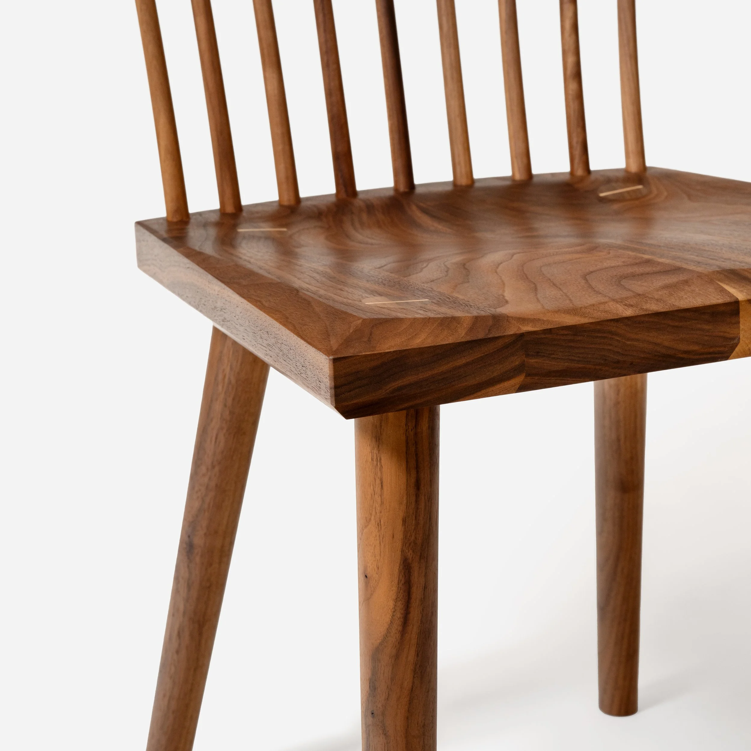 Close-up detail of a sculpted walnut chair seat showing wedged tenon joinery and beveled edges.