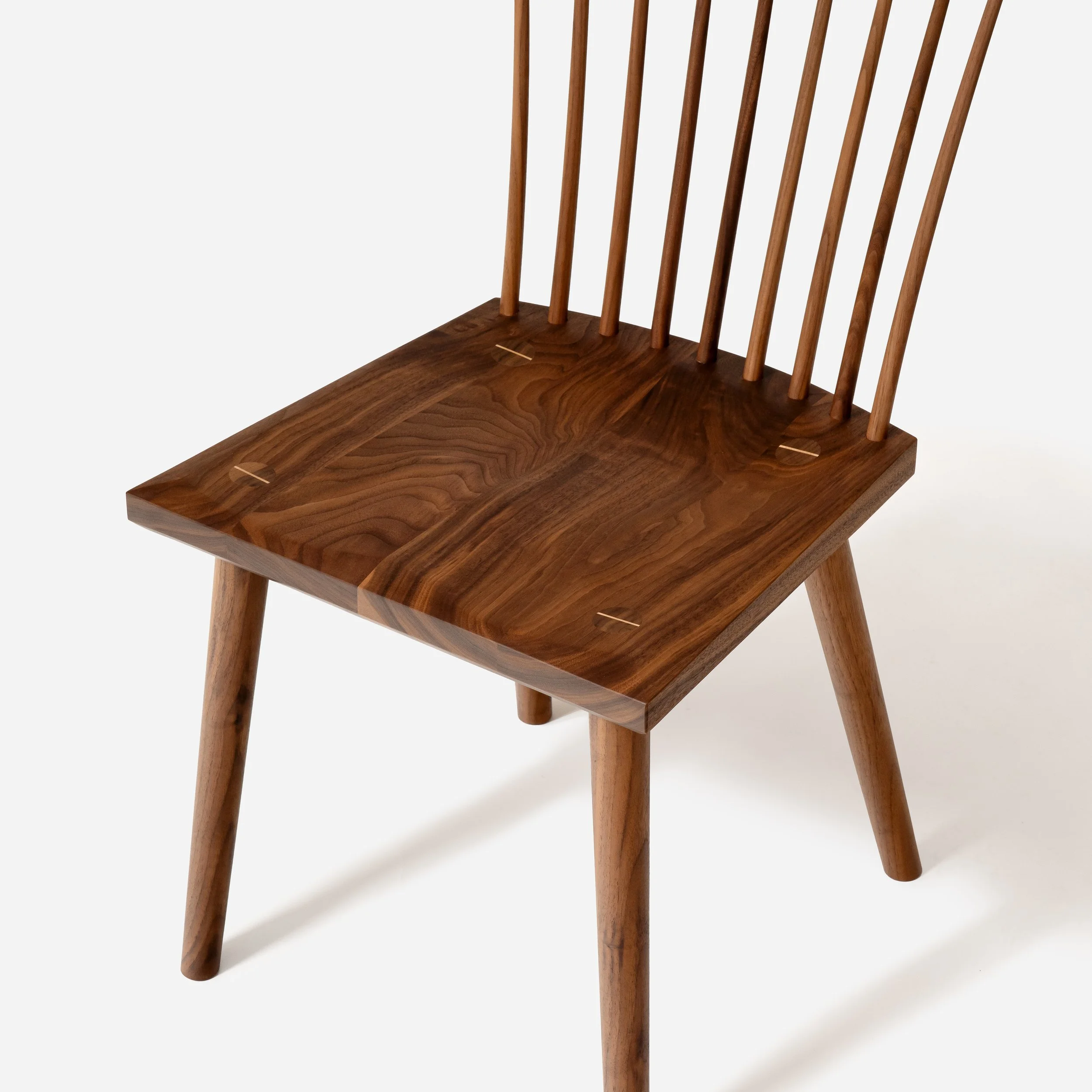 Top-down view of a solid walnut chair seat highlighting natural wood grain and contrasting joinery pins.