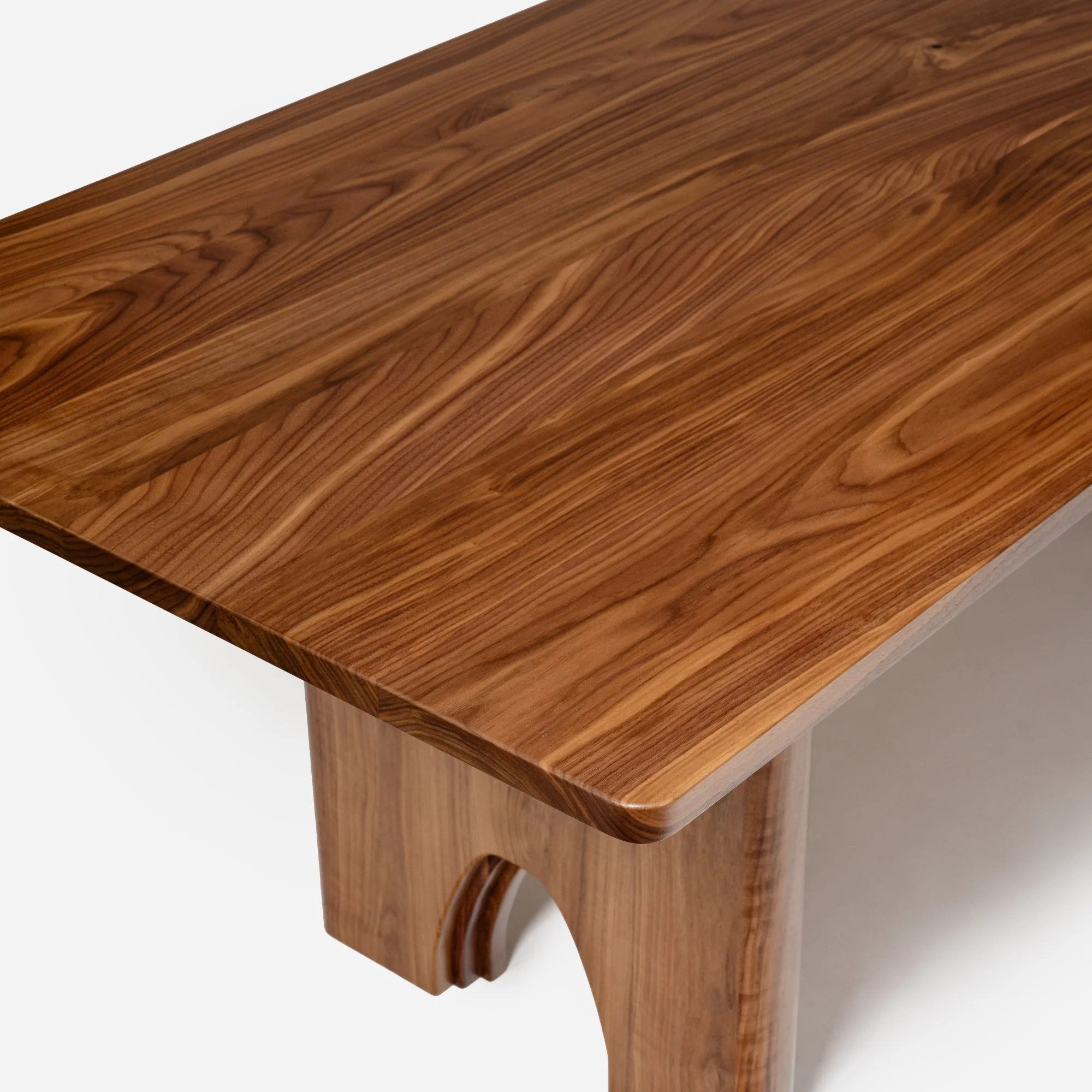 Solid walnut trestle table leg joinery showing substantial mass and sculptural arched design.