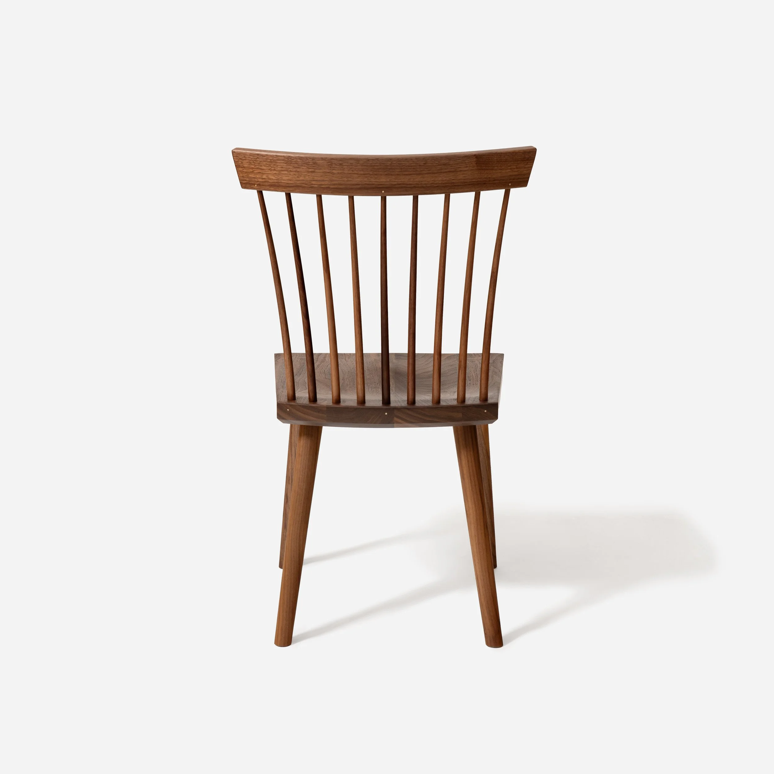 Rear view of a walnut dining chair showing the rhythmic alignment of hand-turned spindles and a curved crest rail.