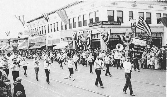 The Santa Ana Polytechnic High School band marching in a parade in front of the Phillips Hutton Building in the early 20th century