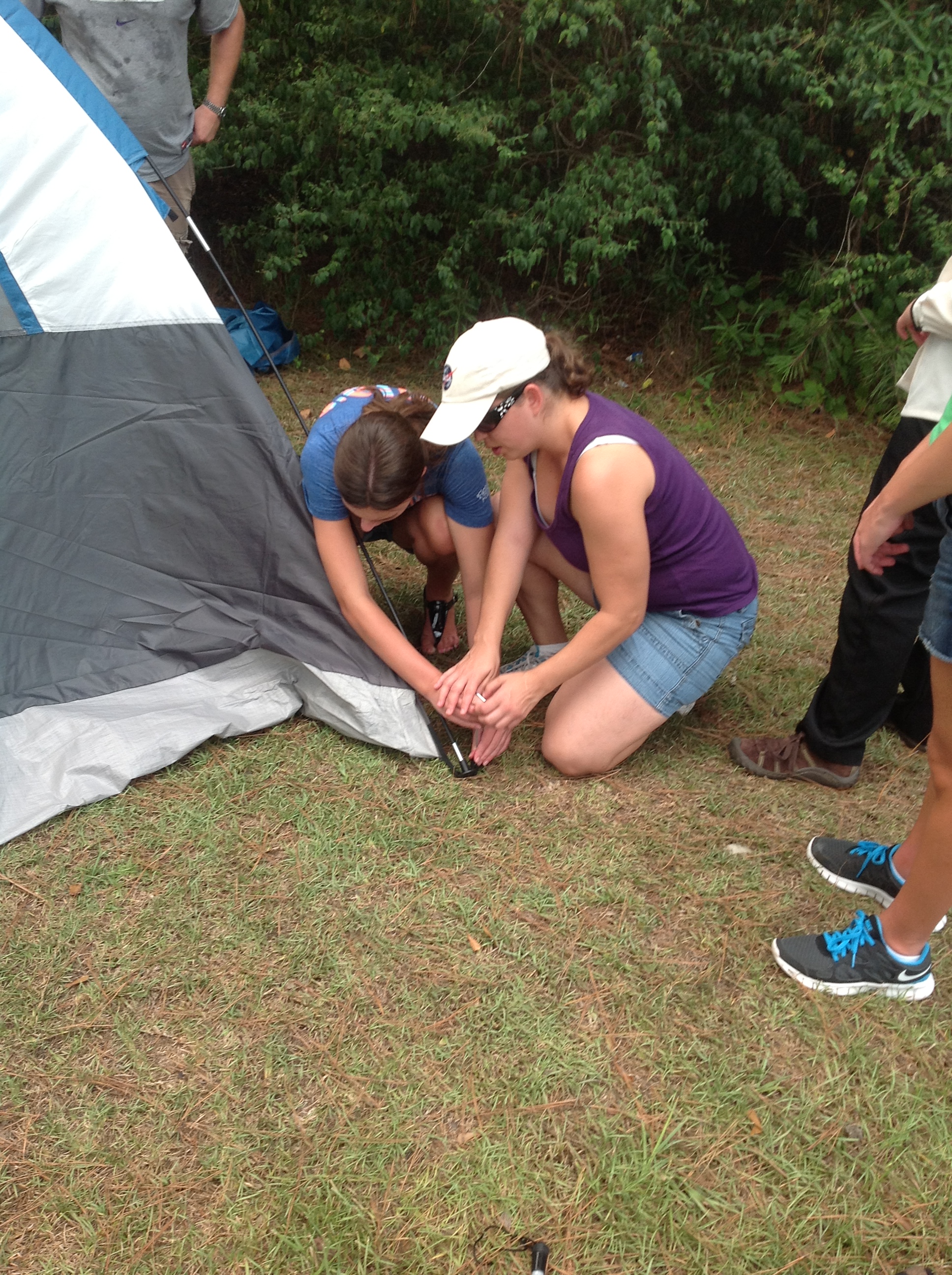 Counselor and student drop the hammer on a tent stake.