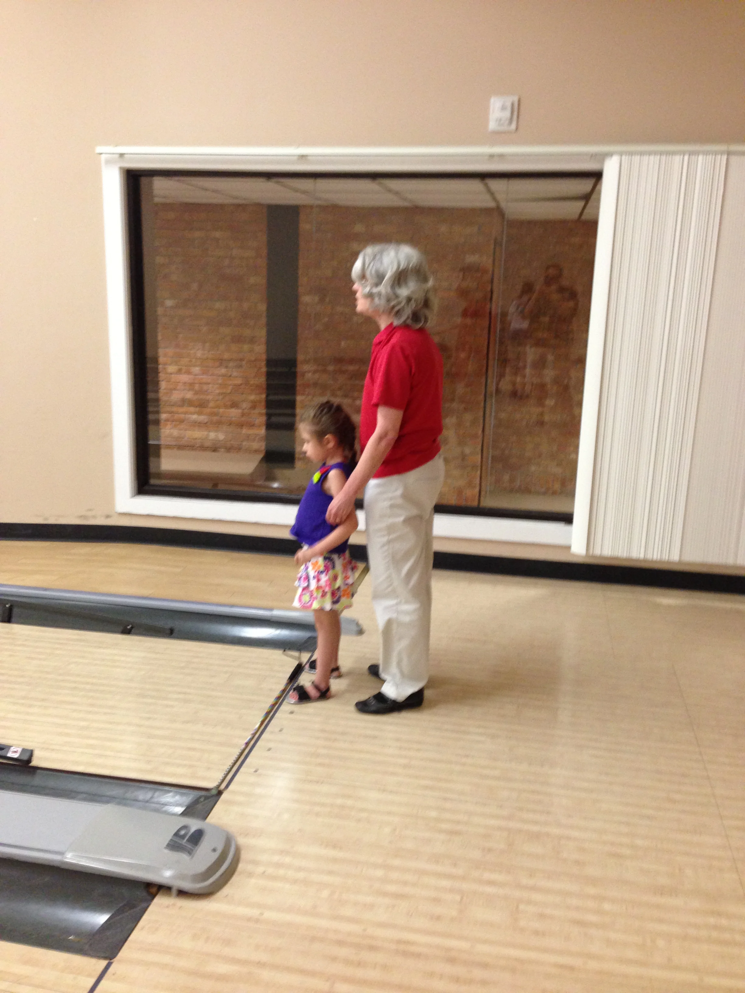 Ms. Sarah waits with Baylee to see how many bowling pins she knocked down