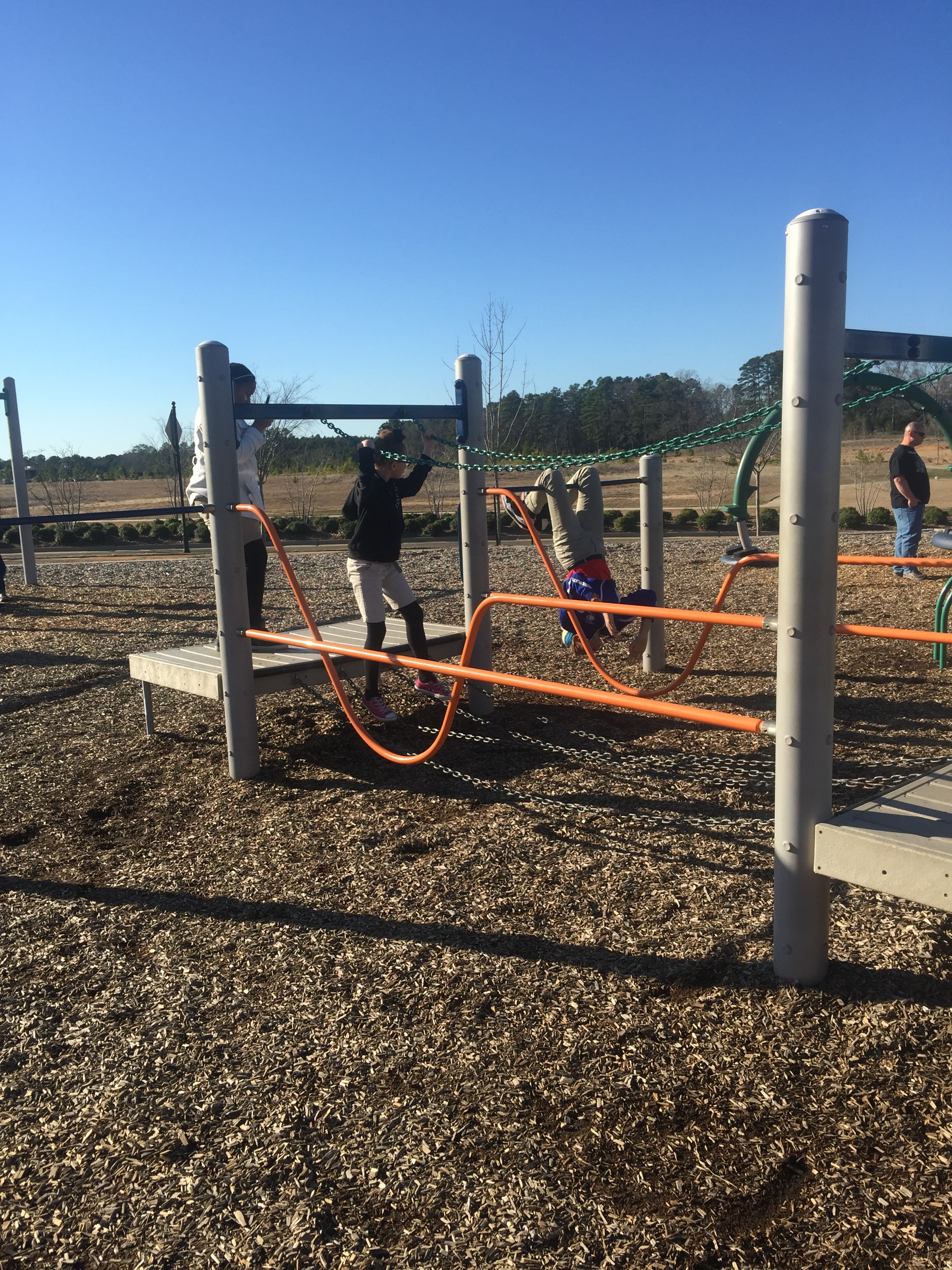 Maniya balances while walking on chains at the playground, and Kiona hangs upside down on a bar.