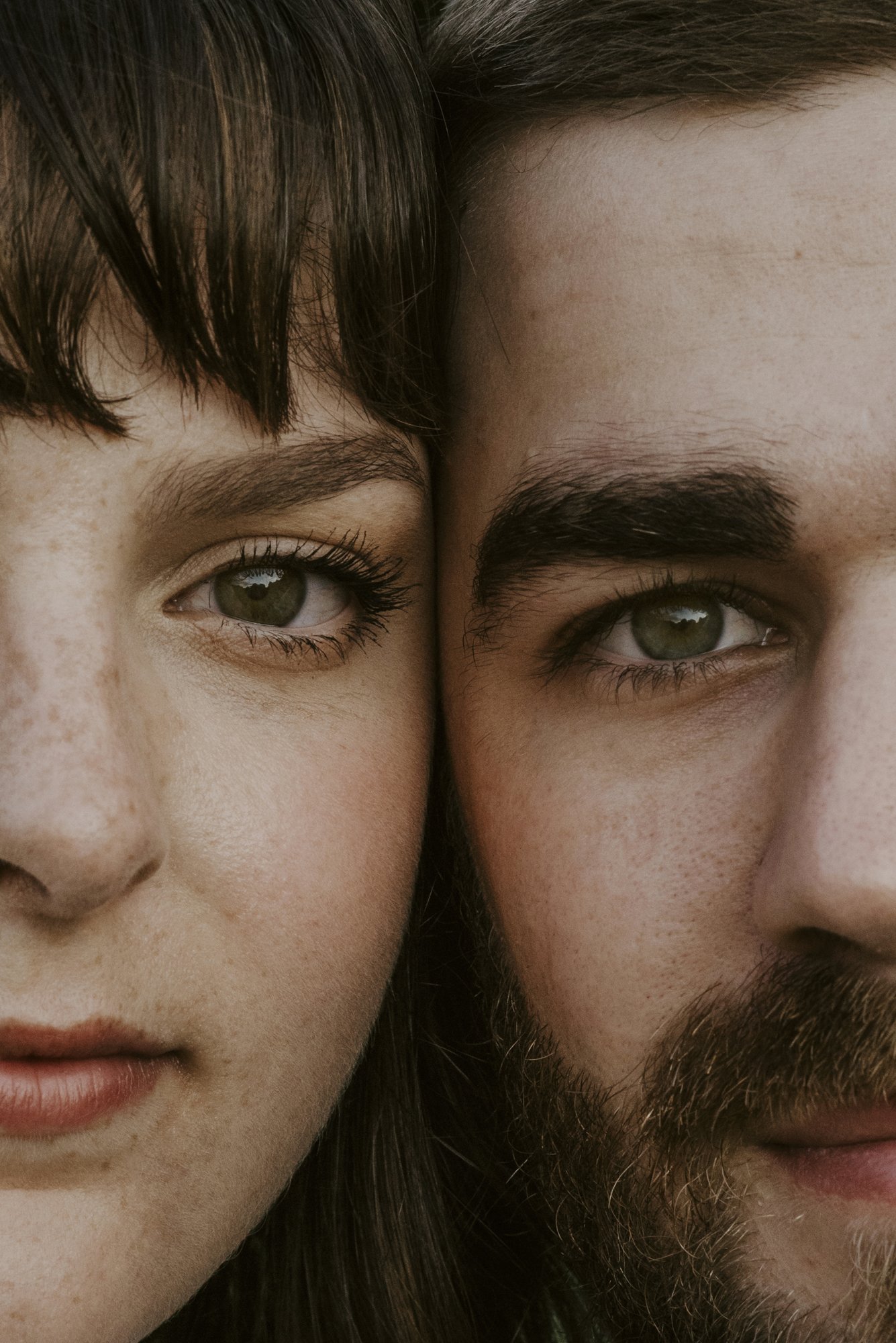 Close-up of two people's faces with their cheeks touching, showing their eyes, eyebrows, and part of their noses. The person on the left has lighter skin and brown hair, while the person on the right has slightly darker skin and brown hair.