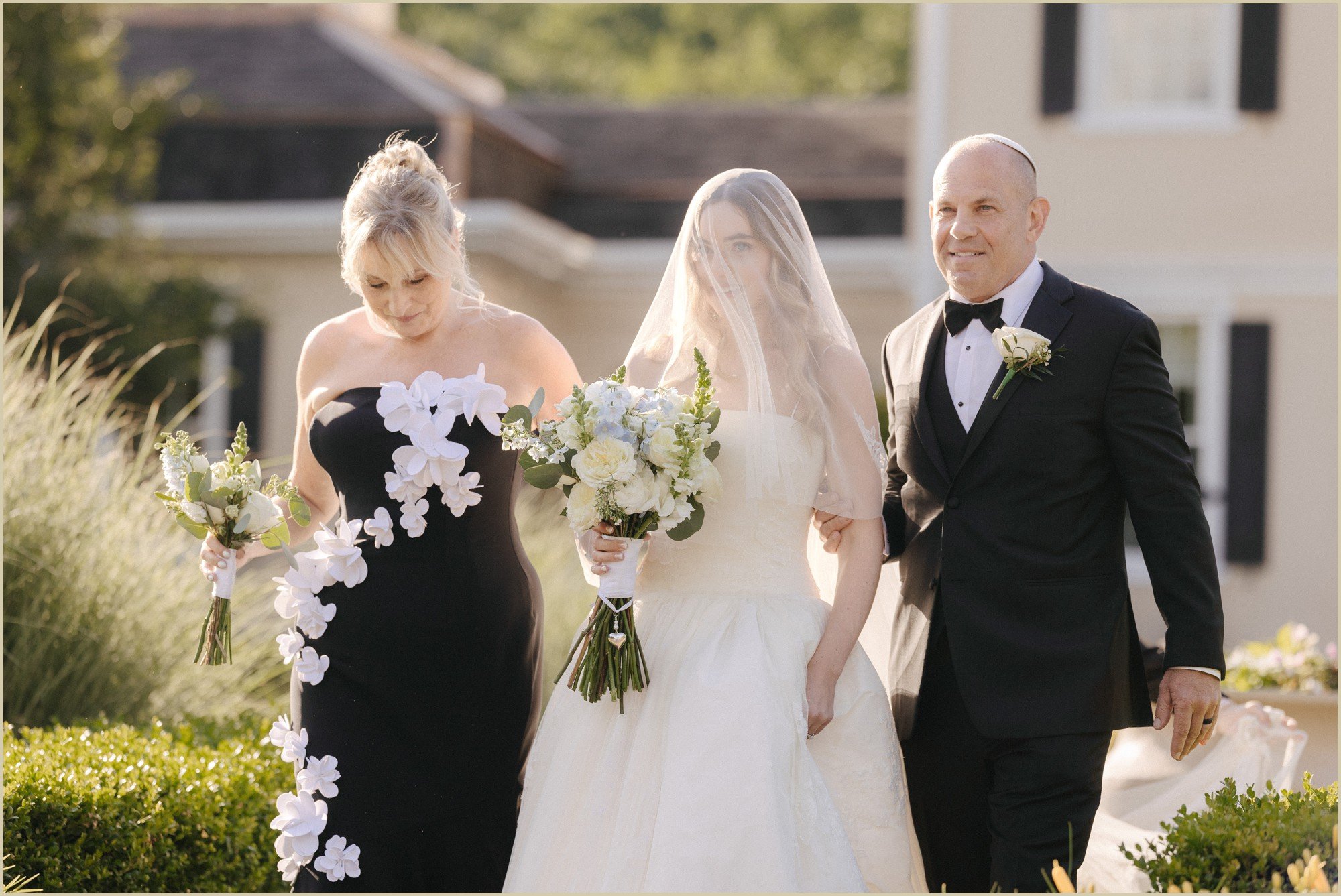 close up of bride walking down the aisle with mother and father with blusher veil