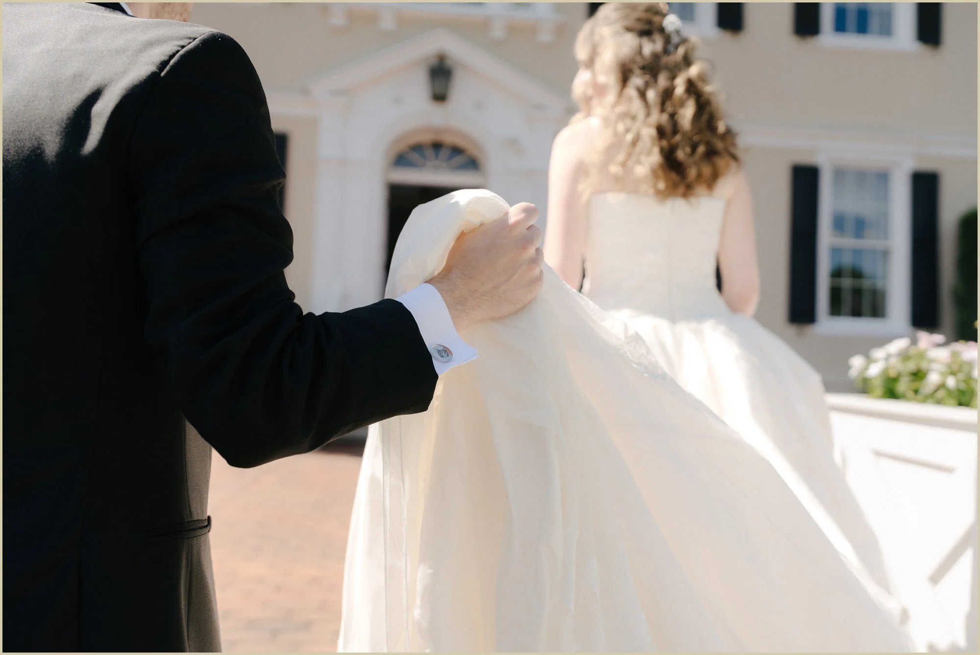 documentary style wedding photo of groom helping hold brides dress