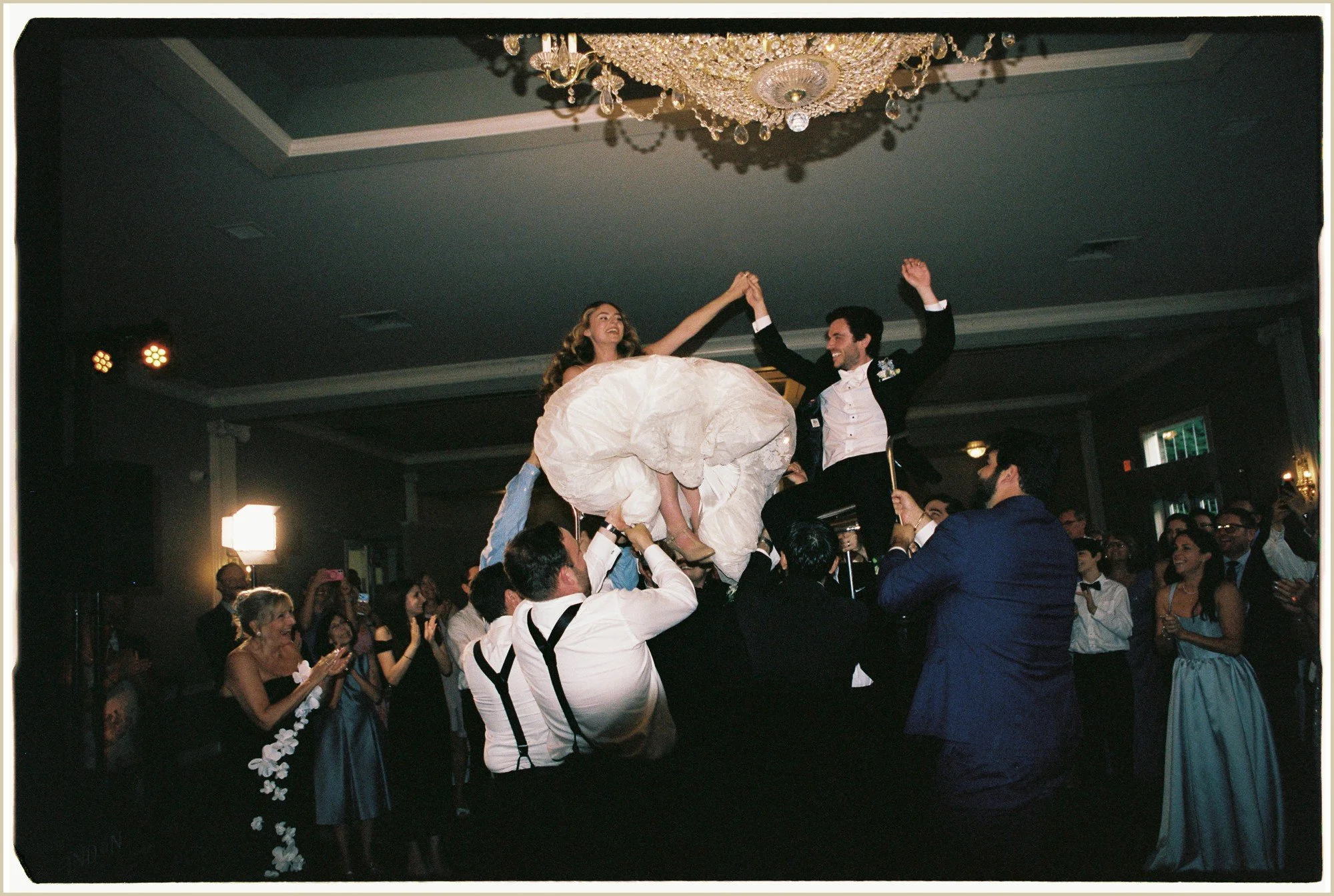 film photo of bride and groom in chairs during the hora