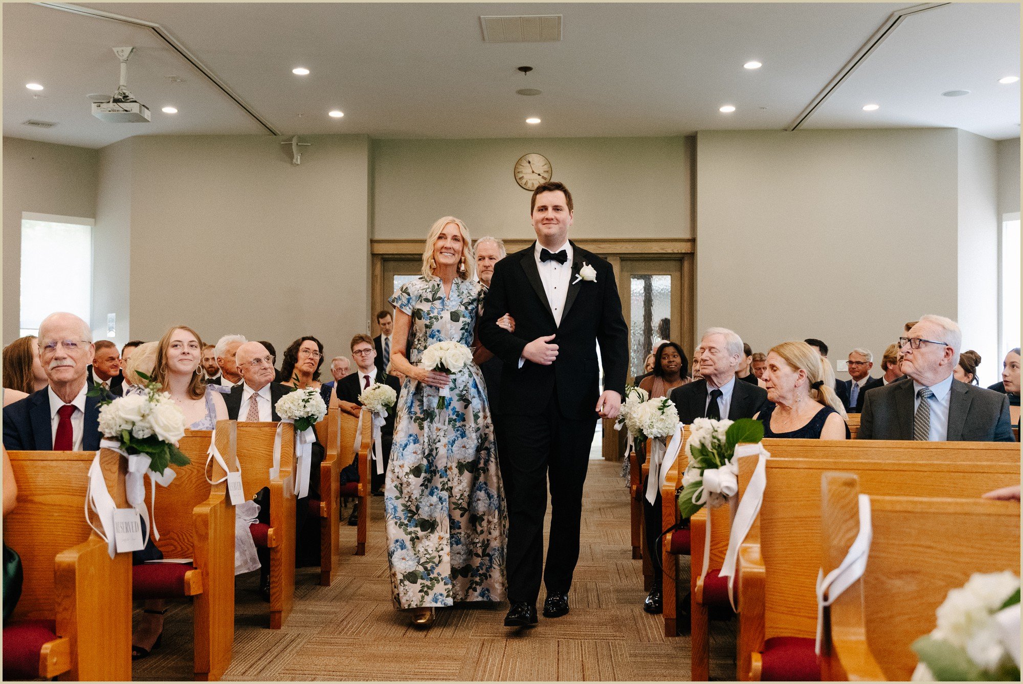 groom walking down the aisle with his mom at church ceremony