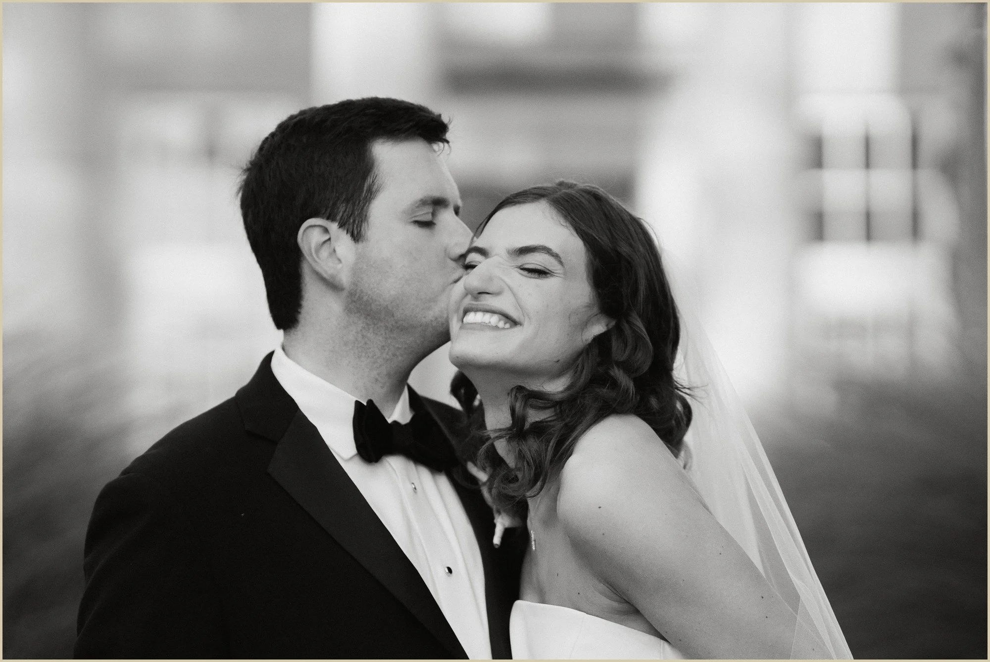 groom kissing his bride on the cheek with the bride beaming