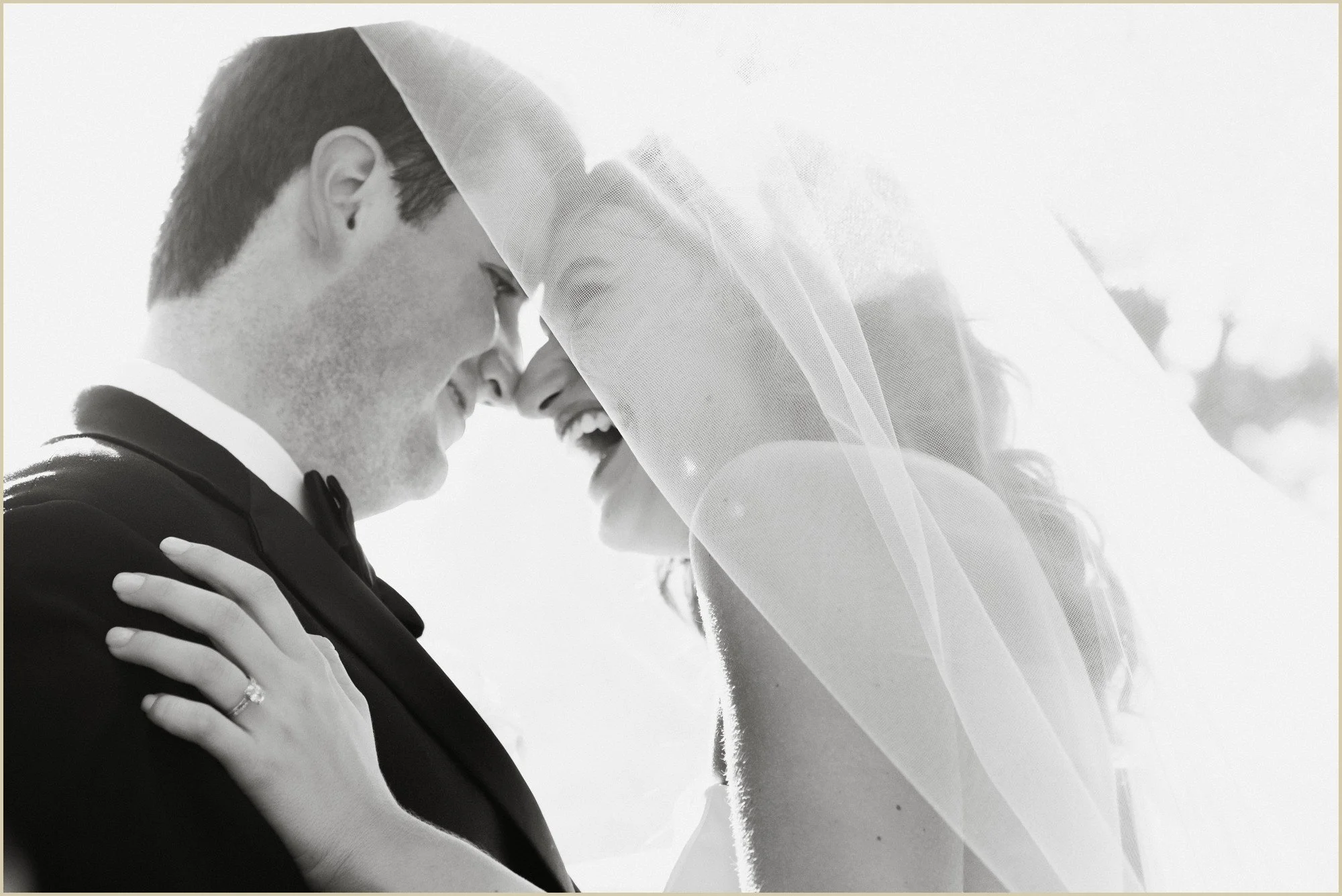 blakc and white candid photo of bride and groom laughing under her veil