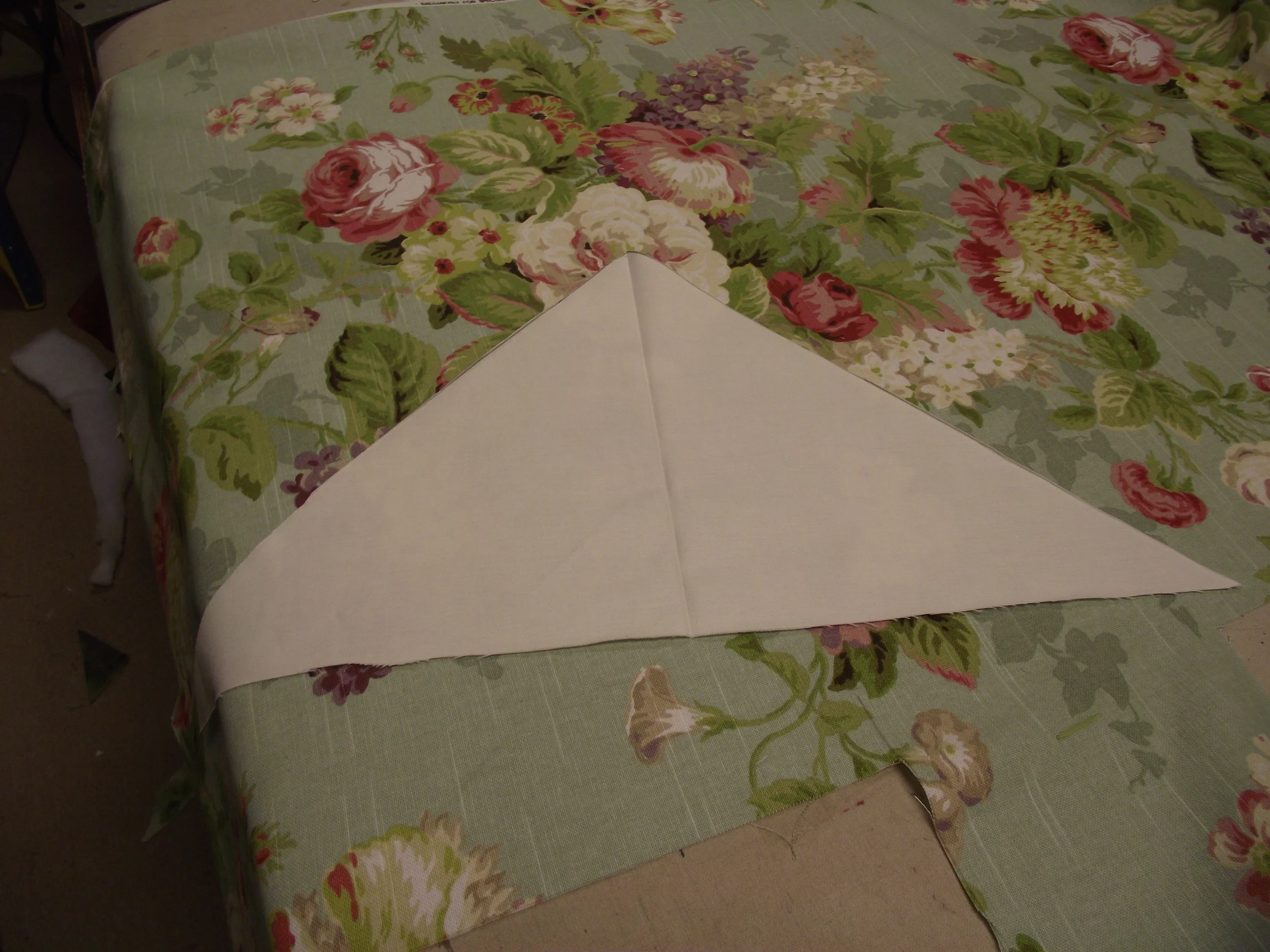 Pattern laid over floral fabric. When Mitering patterns other than stripes it is important to place the pattern properly before cutting. In this example I elected to have the dominate white flower become the center of the finished face piece. Next the triangle was positioned and re-positioned until I had a bold recognizable flower on both the left and right side. This is very important for the effect to work.