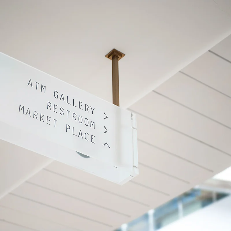 Overhead directional signage in frosted glass, with copper coloured metal frames. 