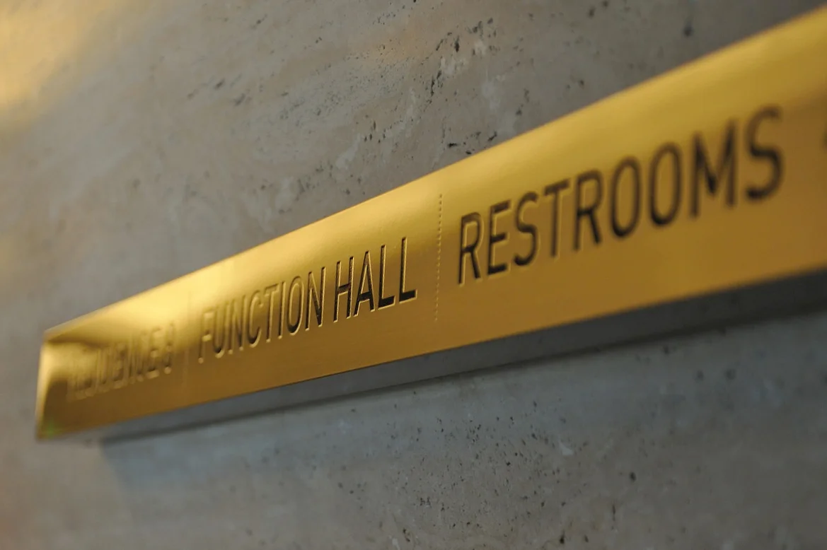 Wall mounted directional signage in common corridors, in etched stainless steel.