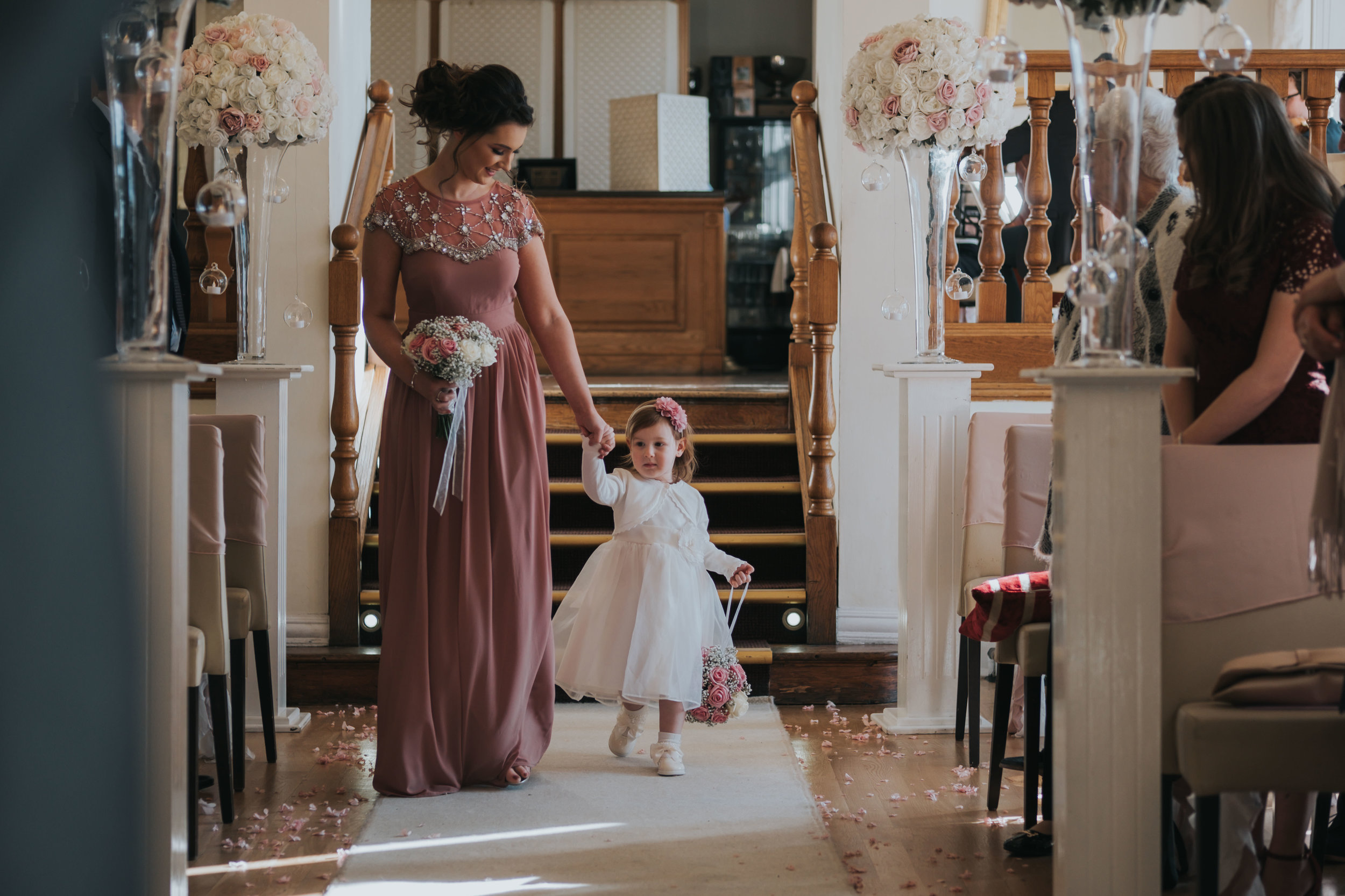 Bridesmaid and flower girl walking down the aisle on their wedding day at west tower exclusive wedding venue in ormskirk