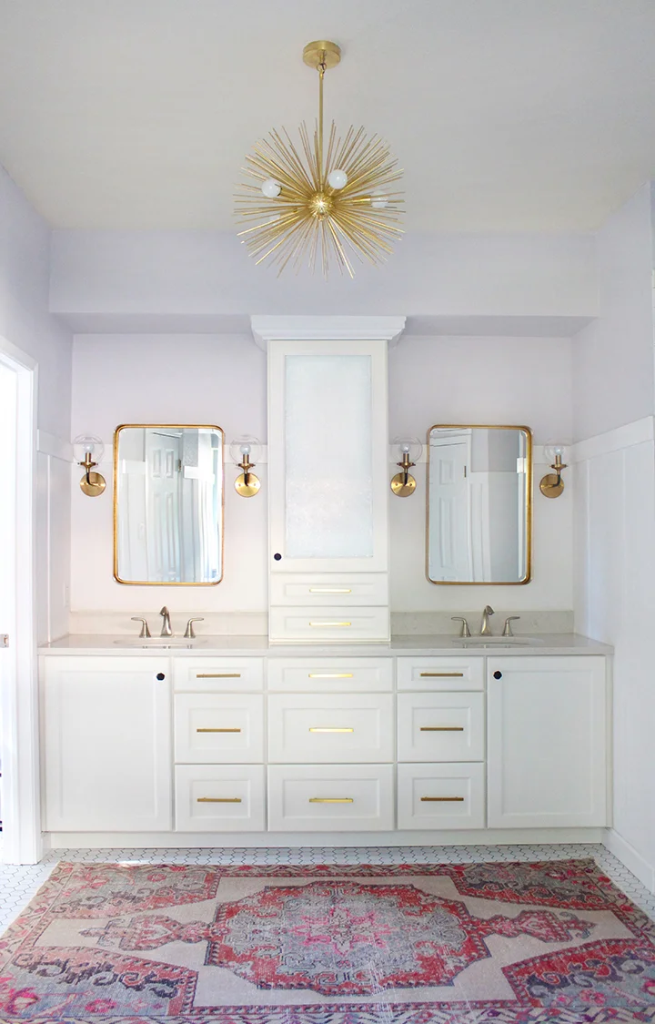  Full bathroom remodel by Kristin Laing Design with white cabinets and gold accents including a brass urchin chandelier. 