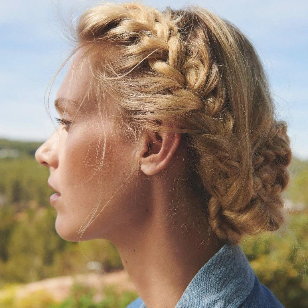 Women with golden blonde hair braided around the head, with a picturesque green field and blue sky background