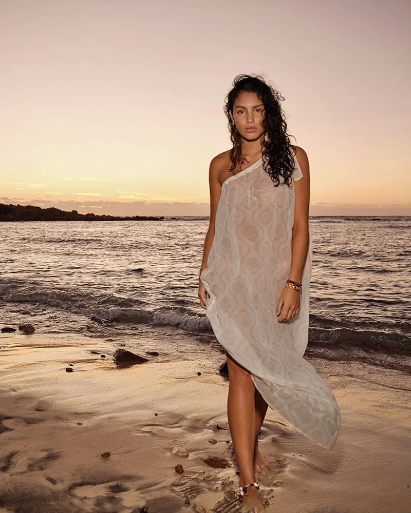 Woman with natural beachy waves walking along the shoreline at sunset, showcasing effortless beach hair styled by the best women’s hair stylist in Paddington at Murphy Gozzard salon.