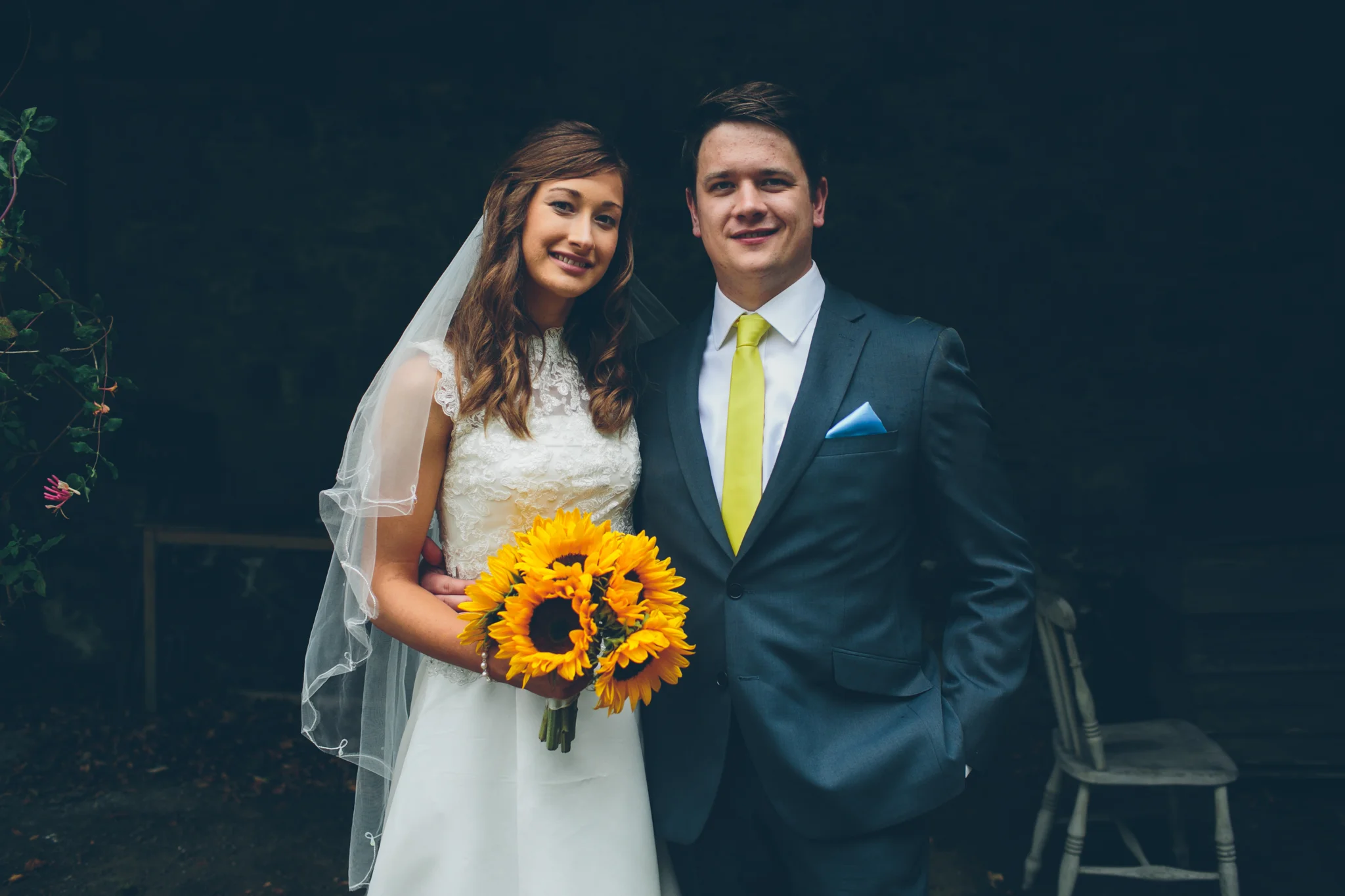 Bride and groom standing outdoors, smiling, with the bride holding a bouquet of sunflowers. Larchfield Estate