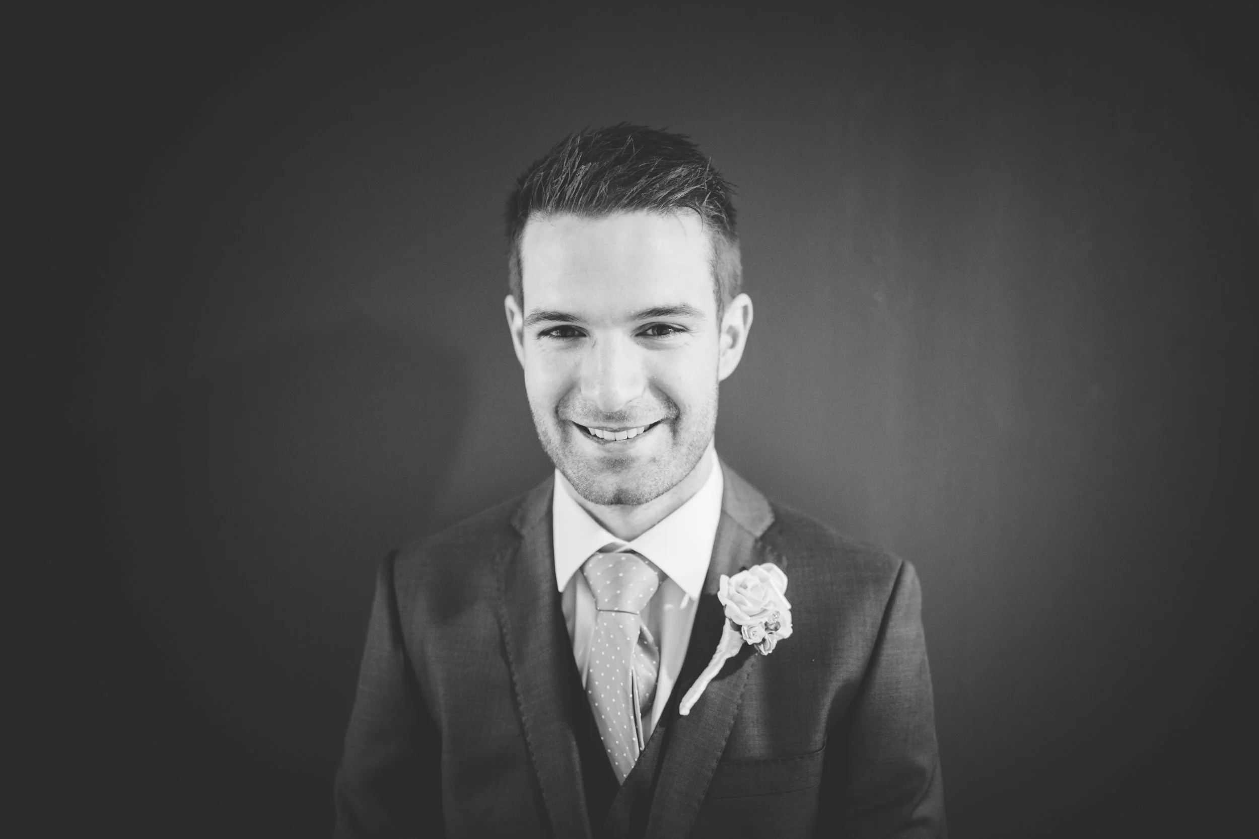 Black and white portrait of smiling young man in a suit with a boutonniere