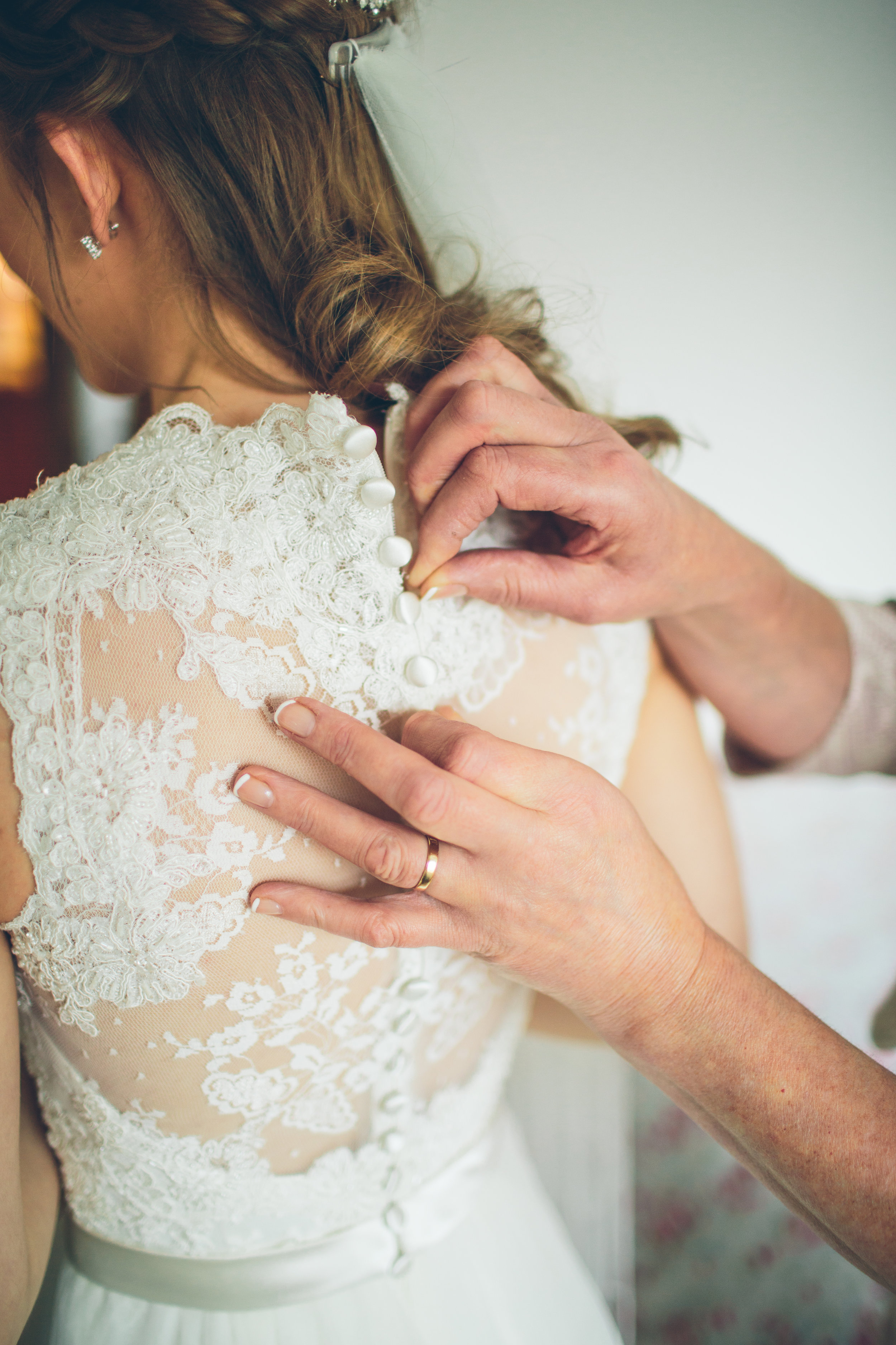 Close-up of a woman in a wedding dress being buttoned up, with someone helping her fasten the buttons on the back of the dress.