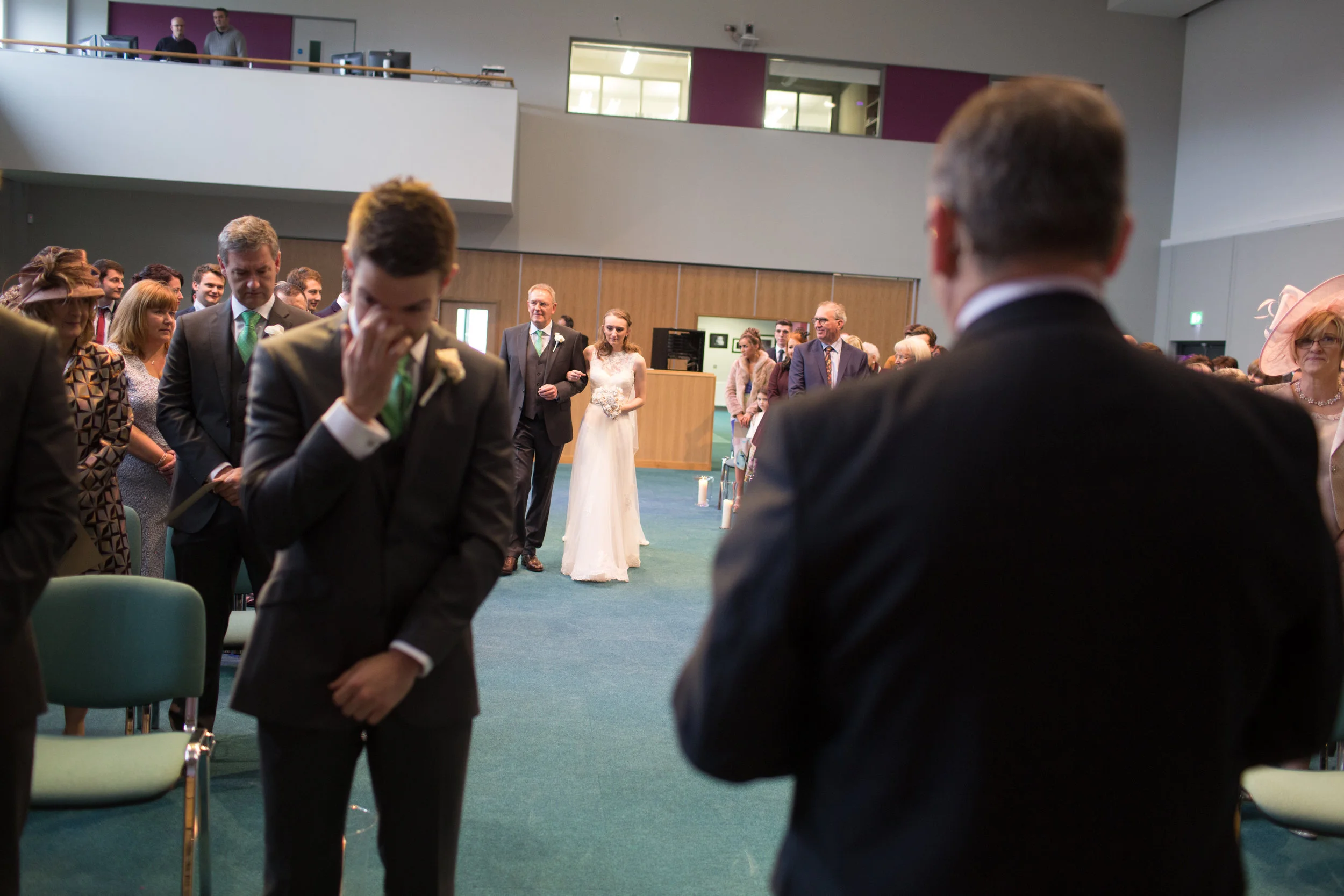 People attending a wedding ceremony in a modern indoor venue with a bride in a white dress walking down the aisle.
