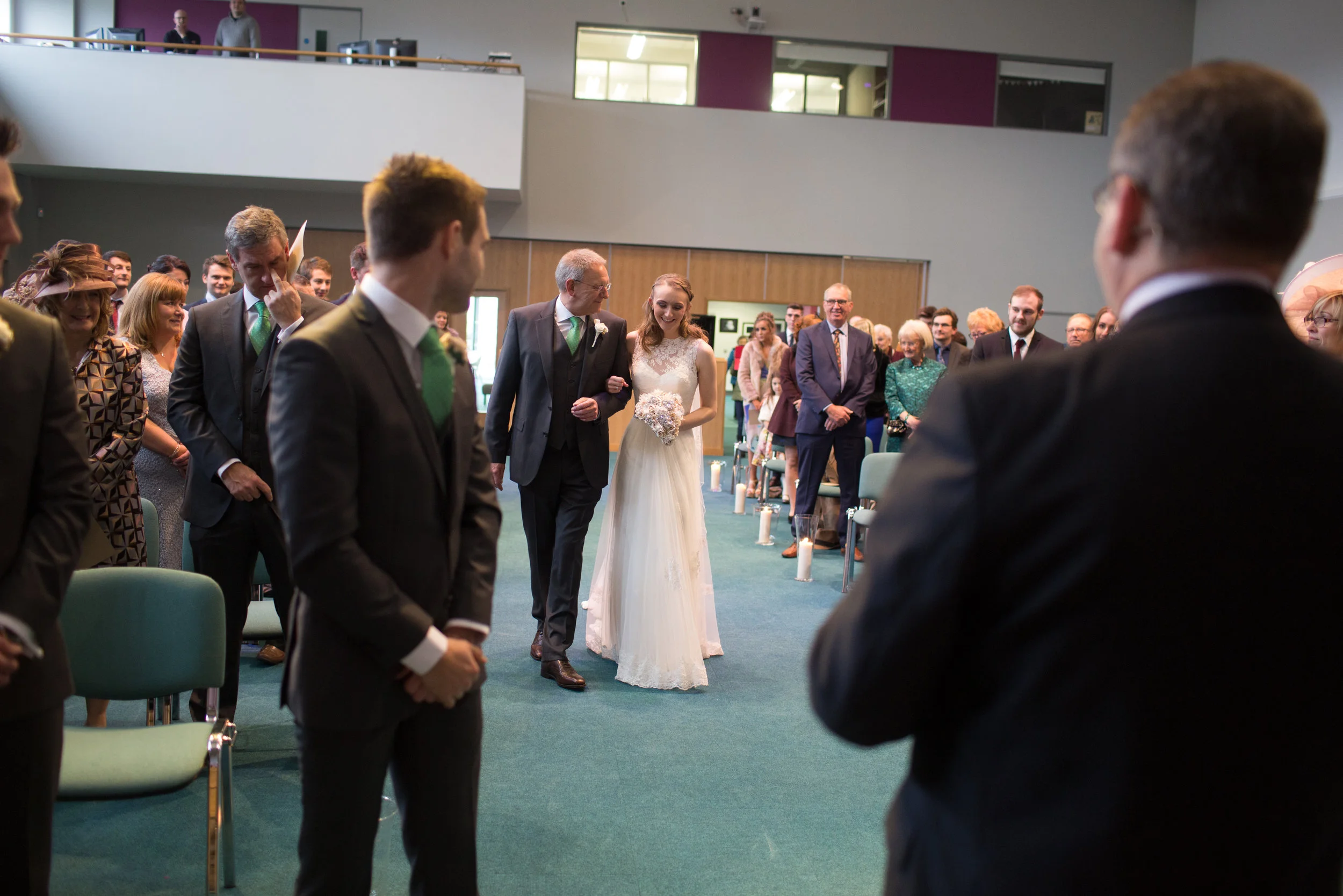 A bride walking down the aisle escorted by her father during a wedding ceremony at a church with guests seated on both sides.
