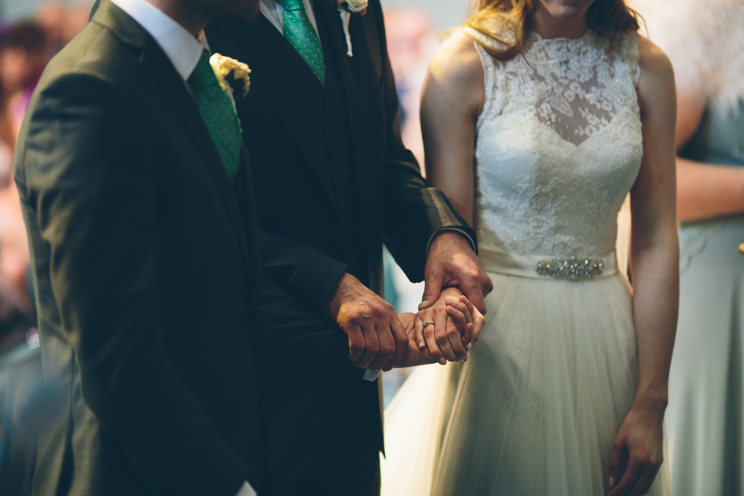 Two men dressed in suits holding hands in a wedding ceremony, with a woman in a wedding dress standing beside them.