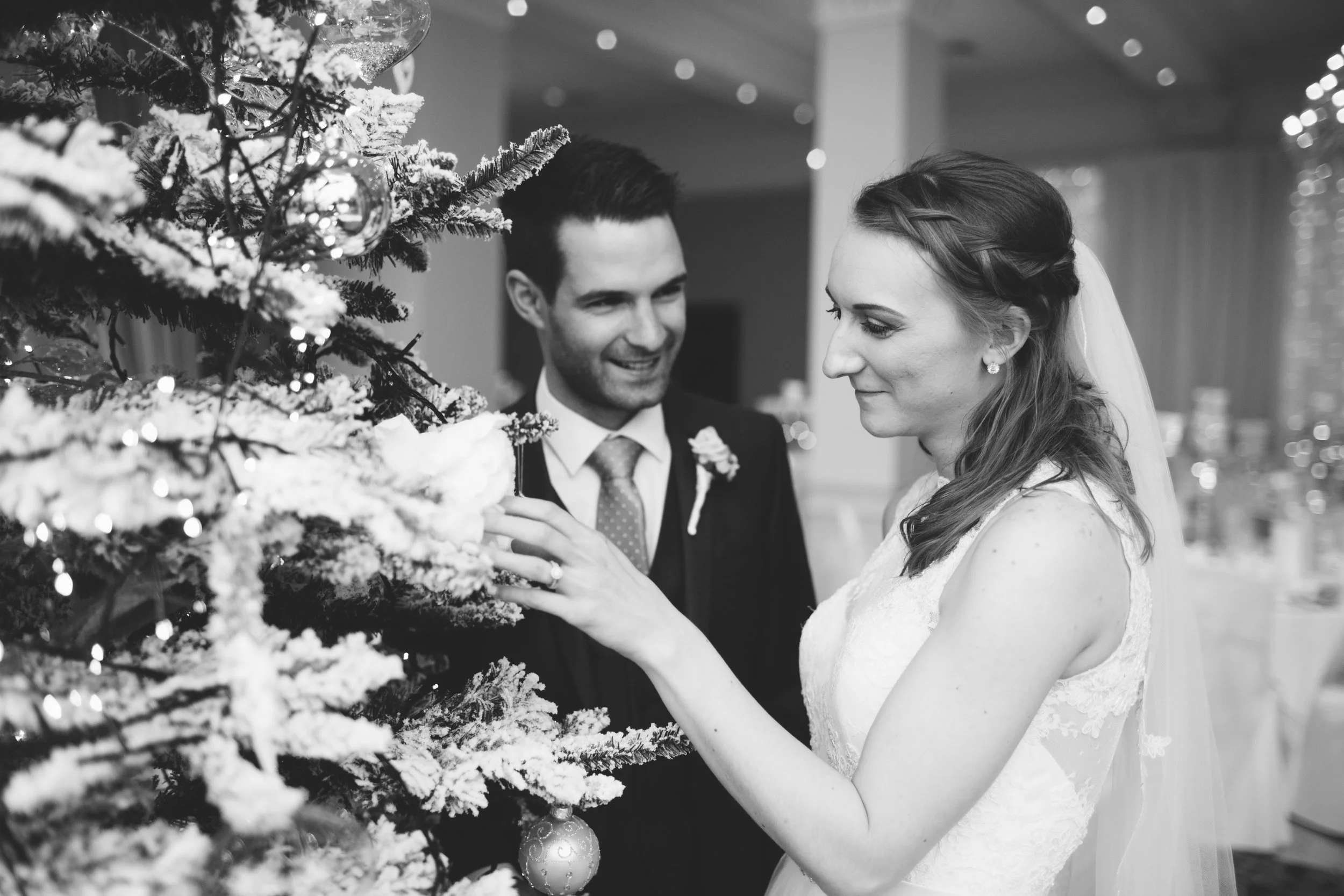 A bride and groom decorating a Christmas tree together at their wedding reception.