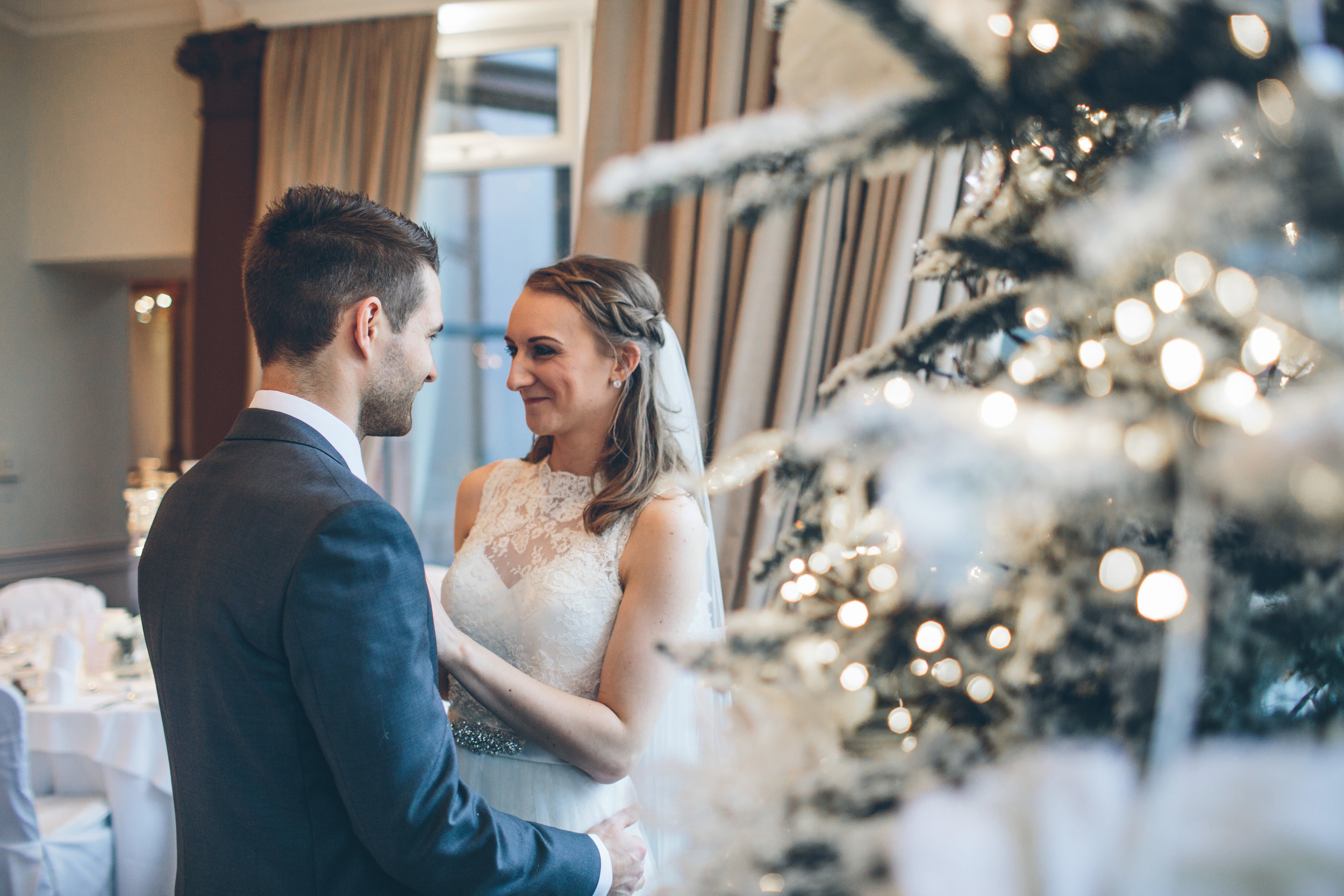 A bride and groom sharing a romantic moment at their wedding reception, with a decorated Christmas tree in the foreground.