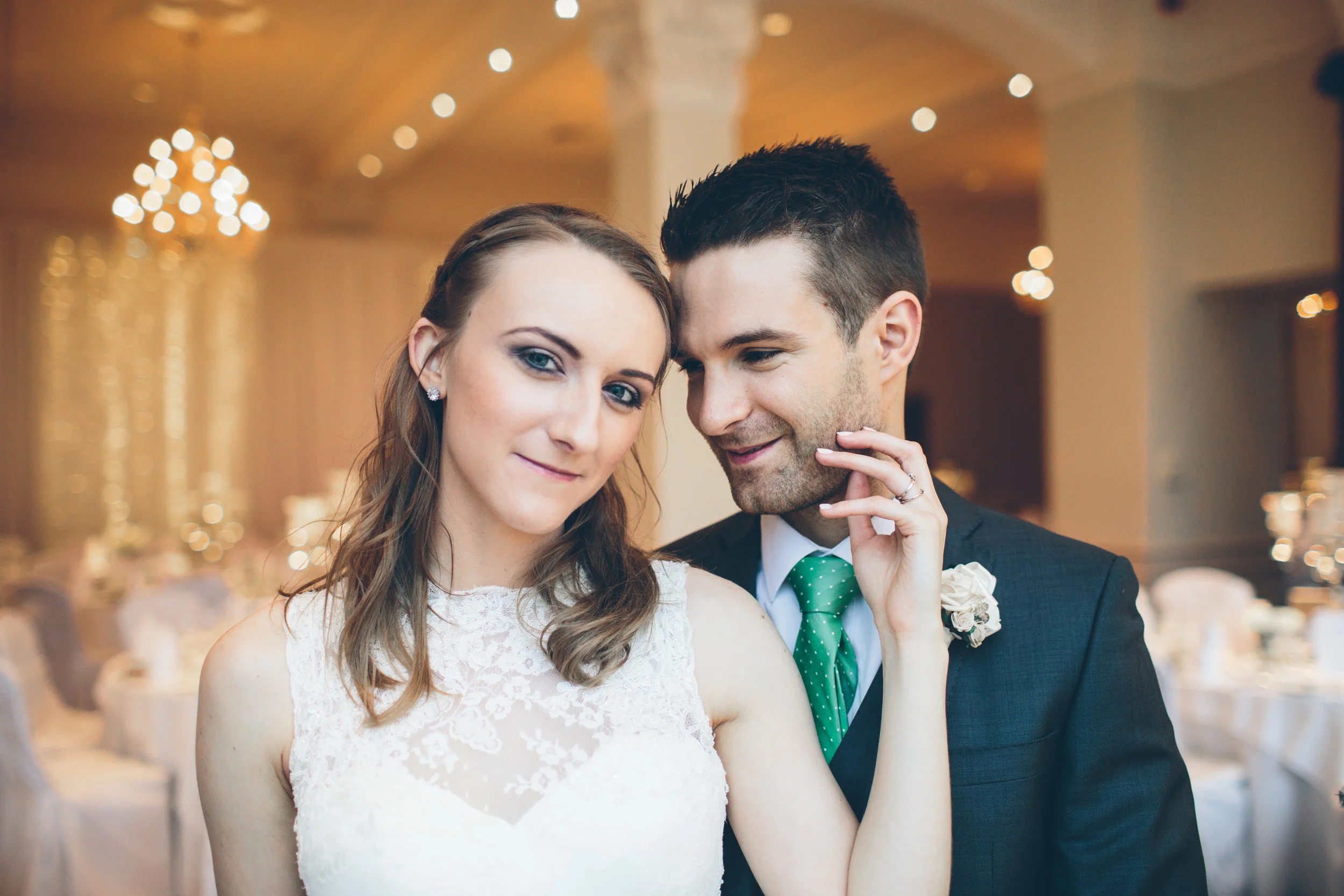 A happy couple at their wedding reception, with tables and soft lighting in the background.