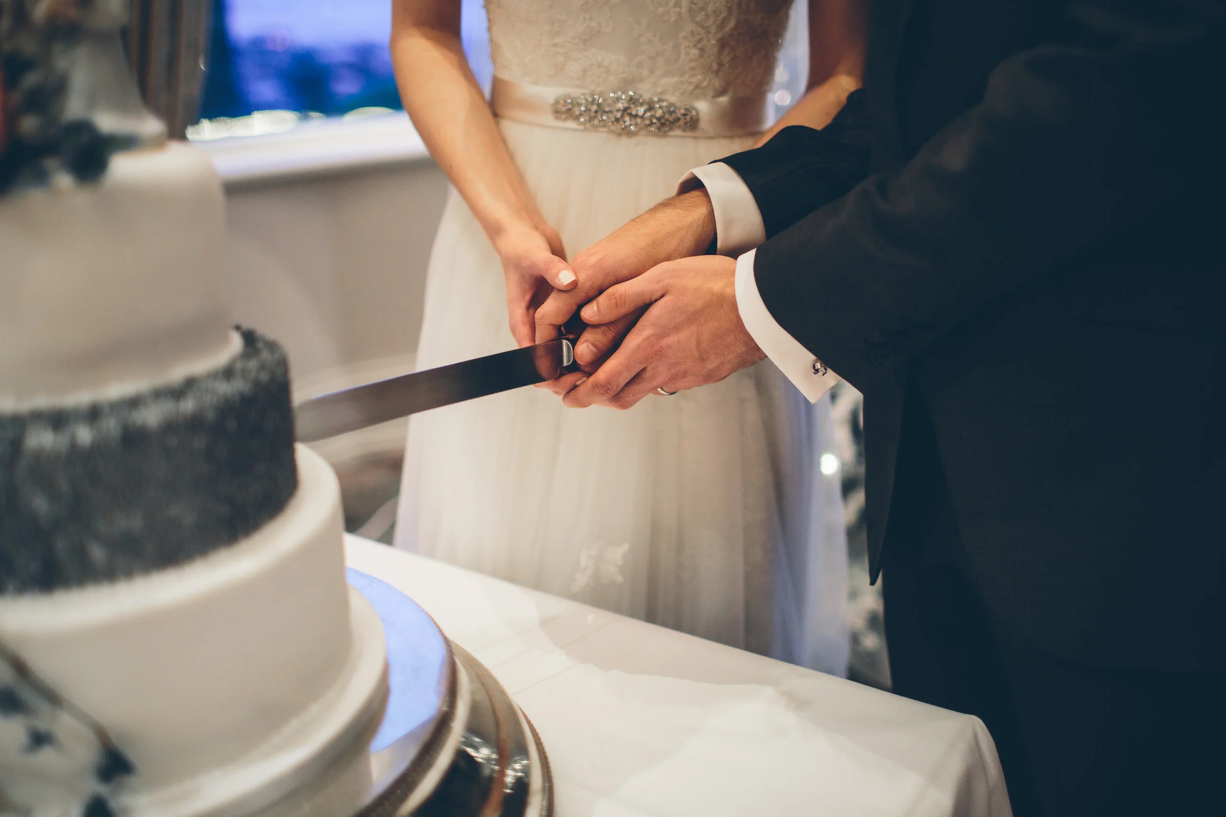 A couple in formal wedding attire cutting a wedding cake together.