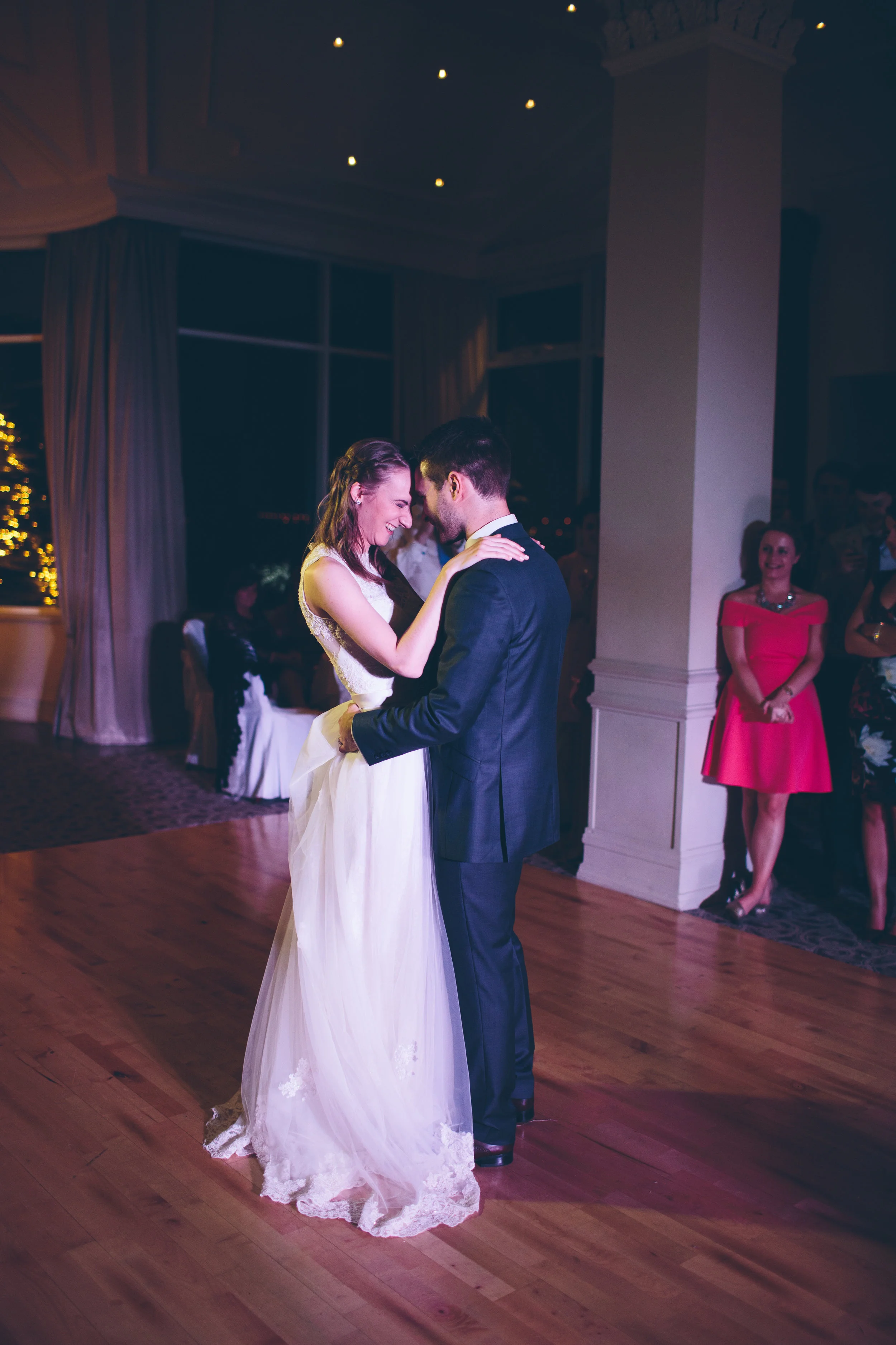 A bride and groom sharing a dance at their wedding reception, with guests watching in the background.
