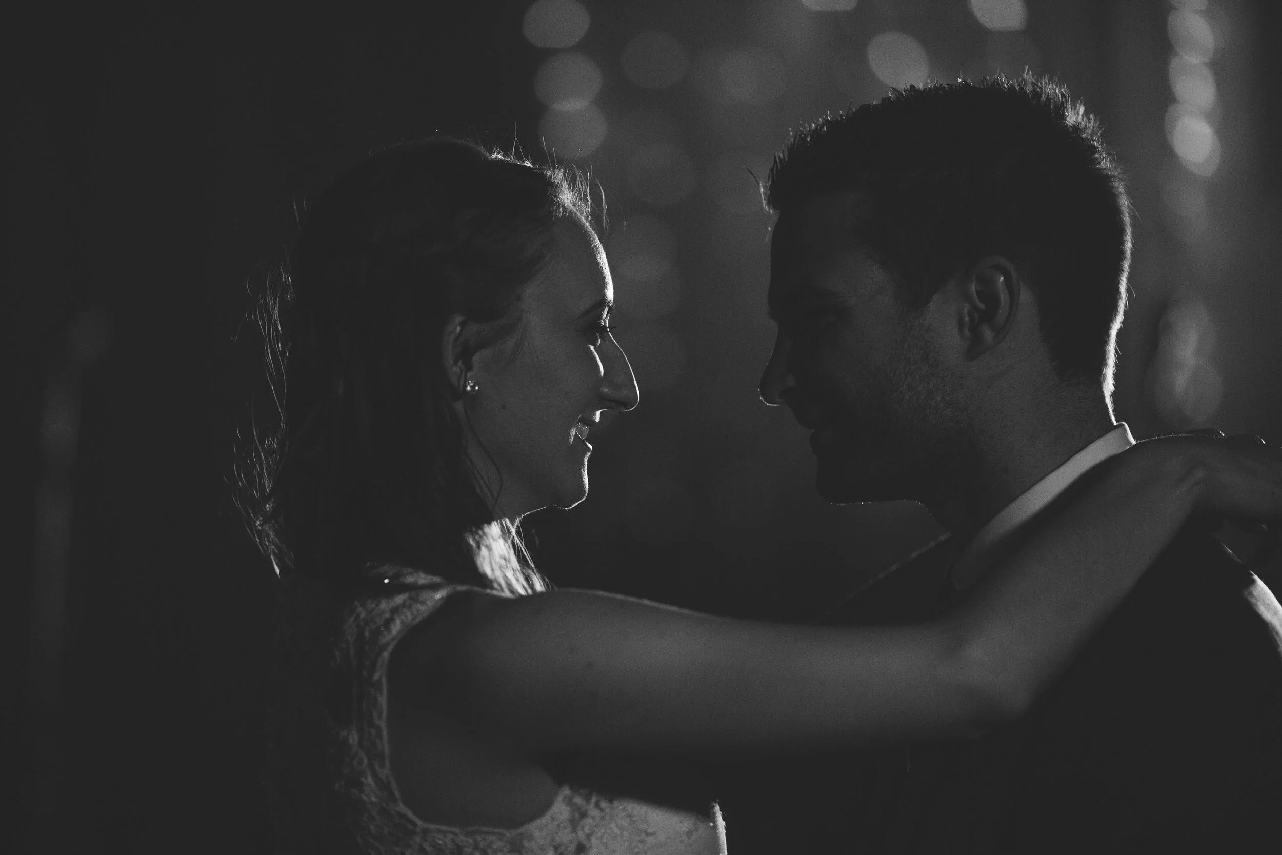 A black and white photo of a smiling couple dancing closely, facing each other with arms around each other's shoulders.