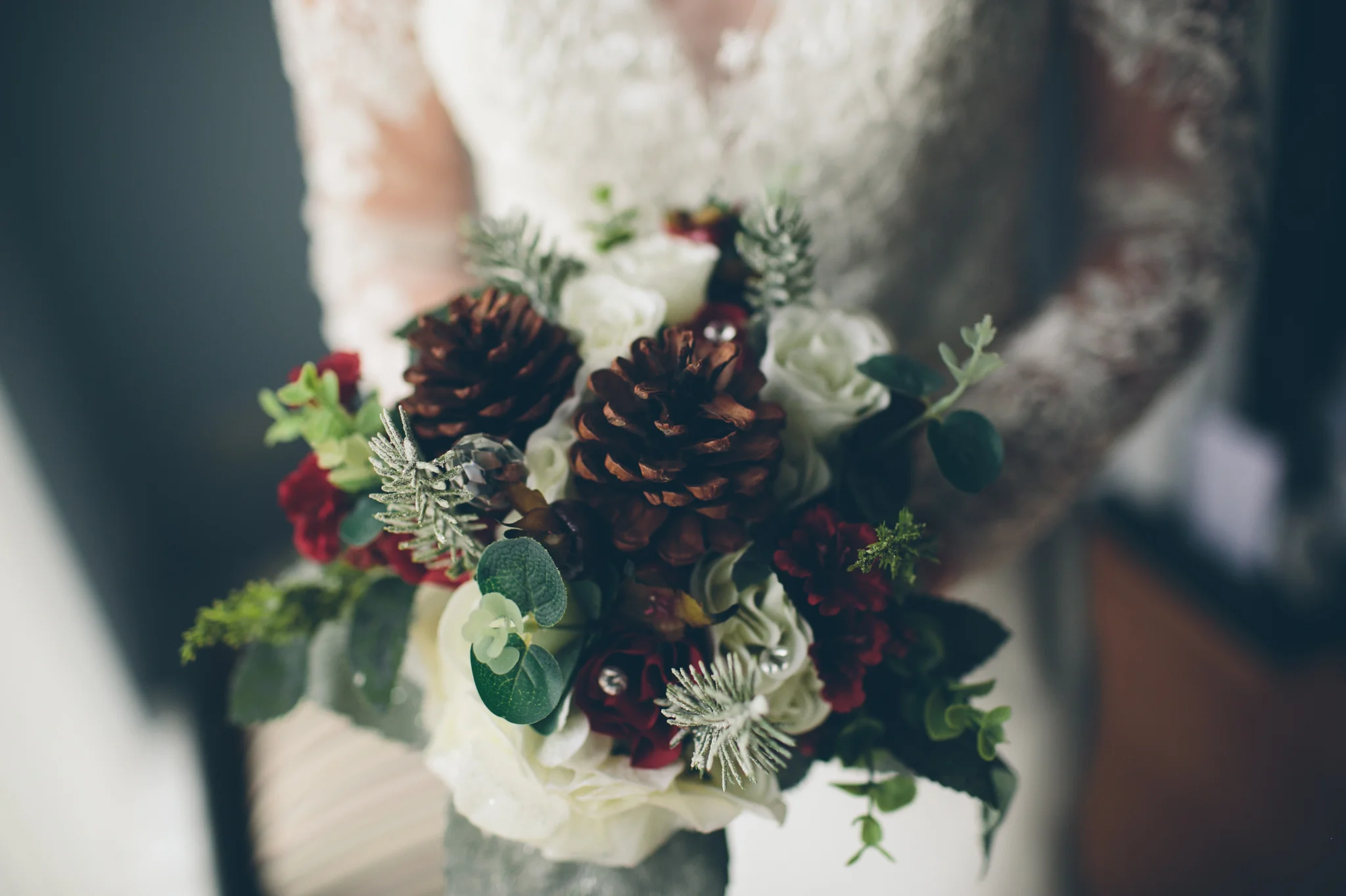 A bouquet with pinecones, white roses, red flowers, green leaves, and silver accents.