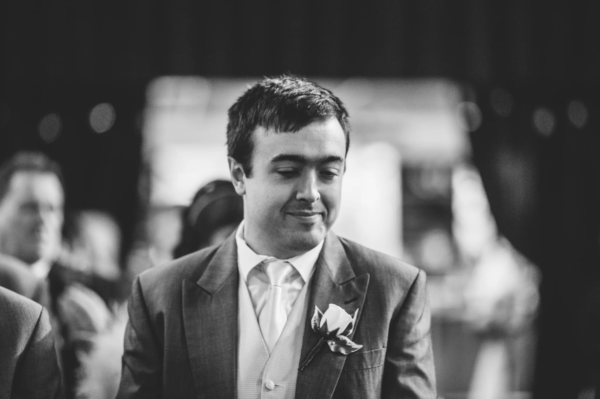 Black and white photo of a young man in a suit with a boutonnière, smiling softly.