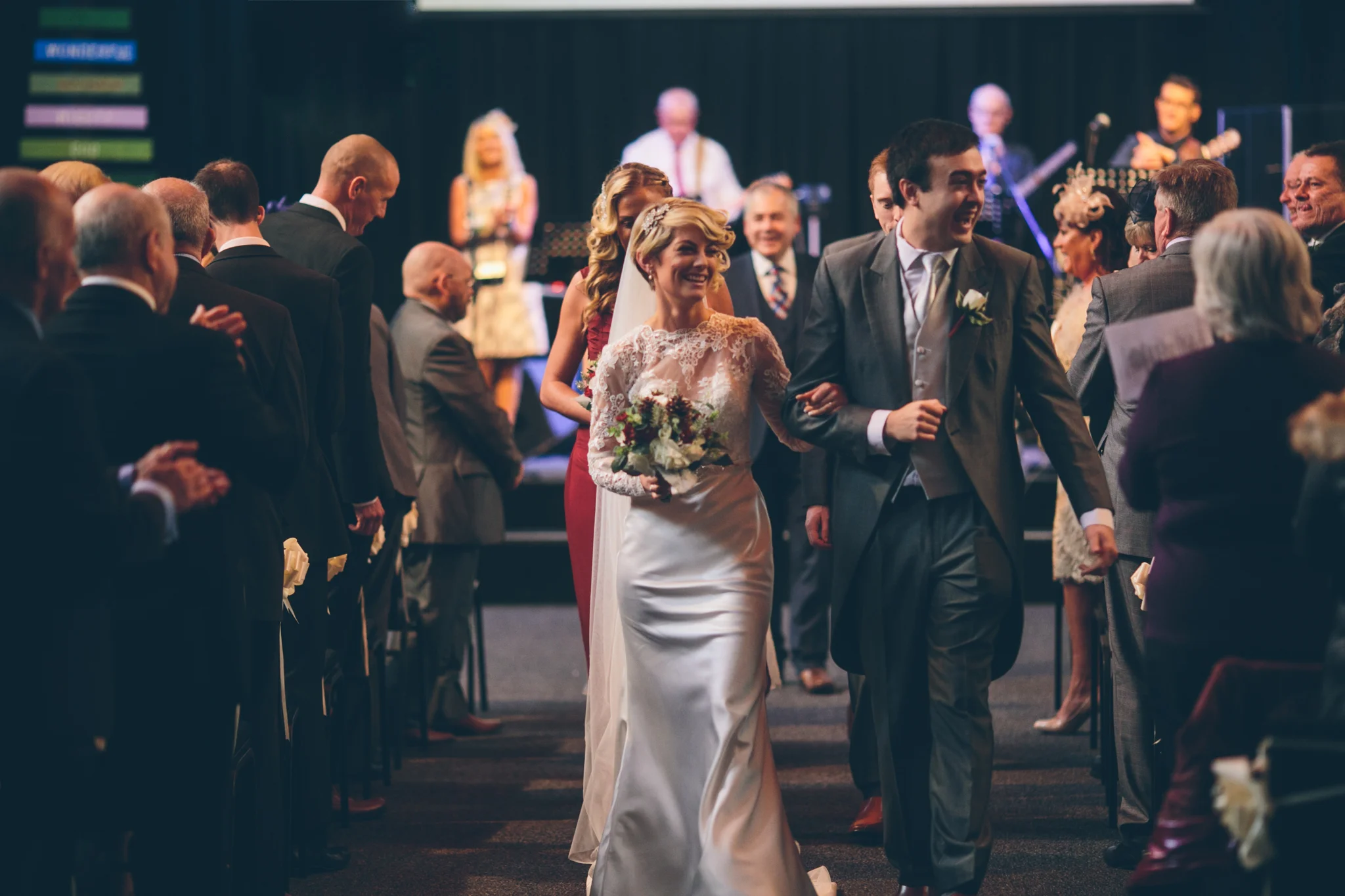 Bride and groom walking down the aisle at their wedding while guests applaud.