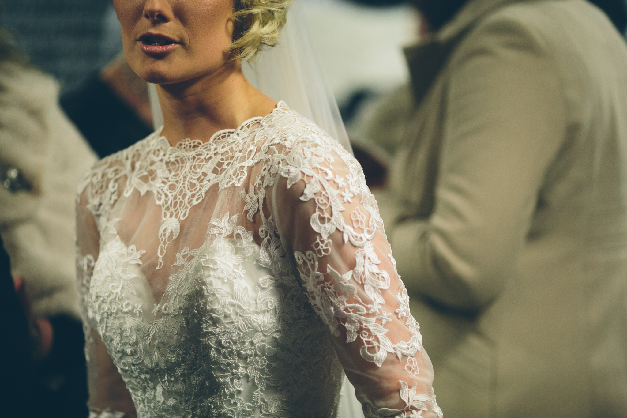 Close-up of a bride wearing a lace wedding dress with intricate floral patterns, at a wedding ceremony.
