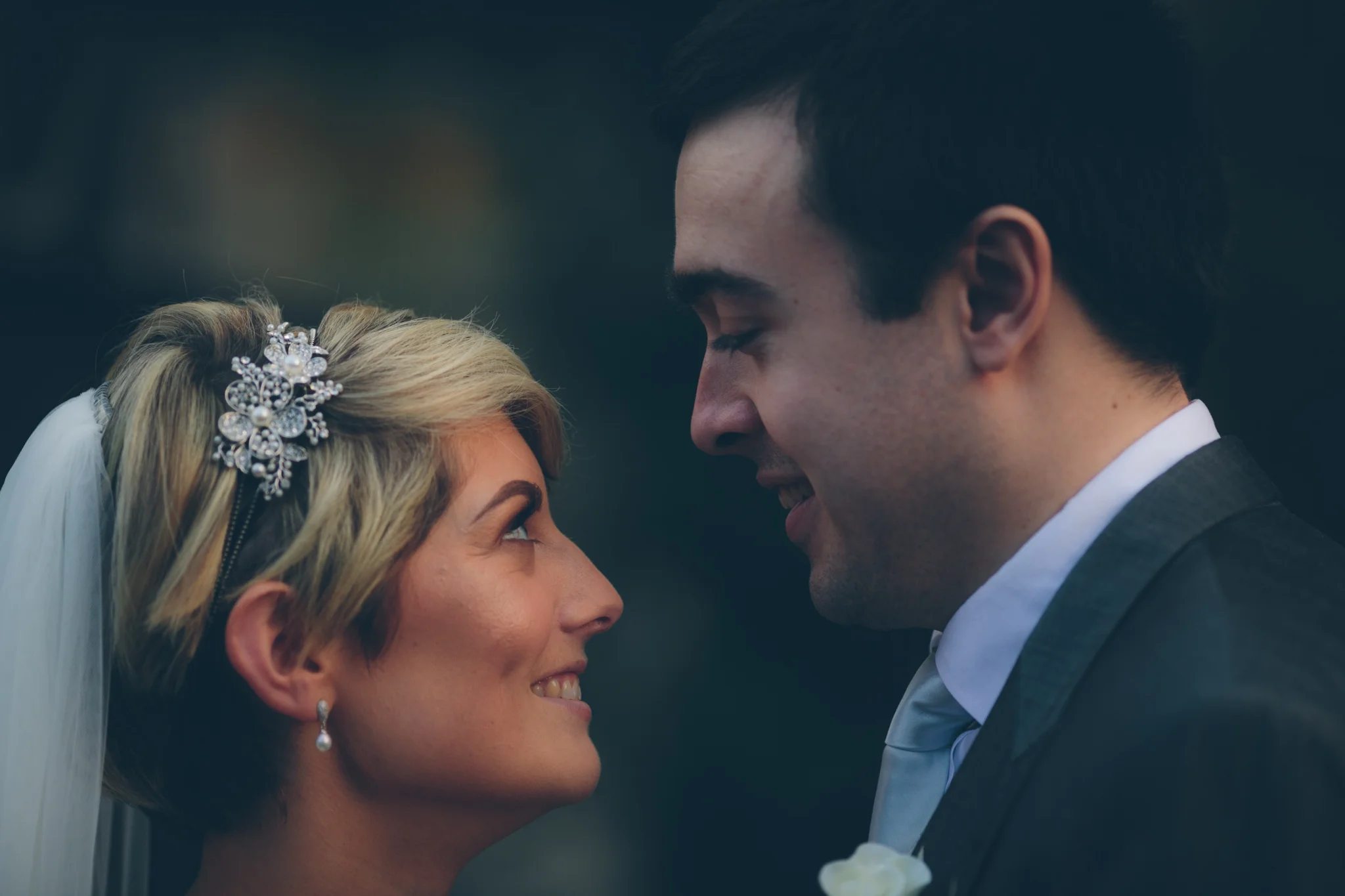 A bride and groom face each other close-up during their wedding, smiling and looking into each other's eyes.