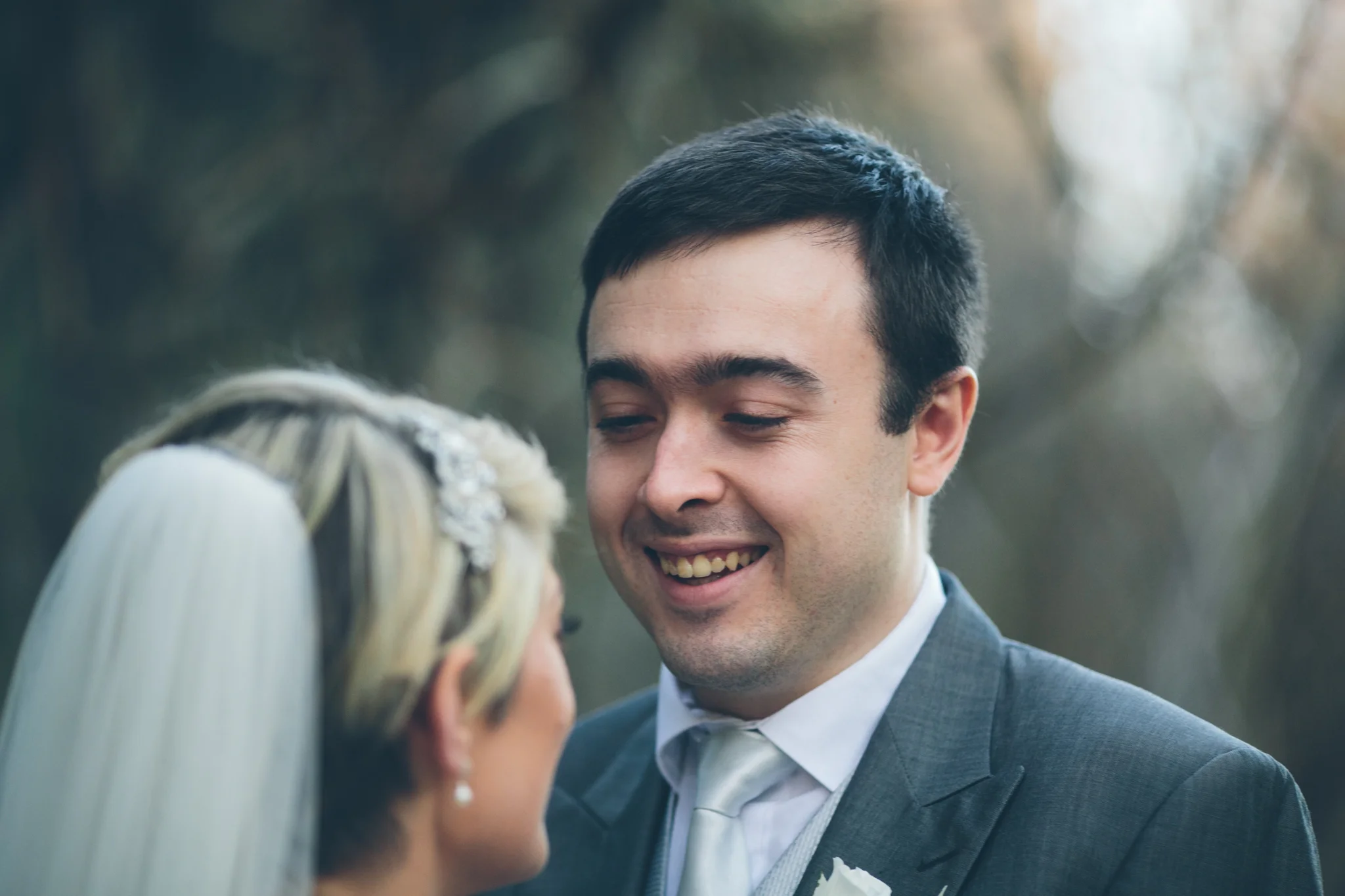 A groom smiling at a bride during their wedding outdoors in nature.