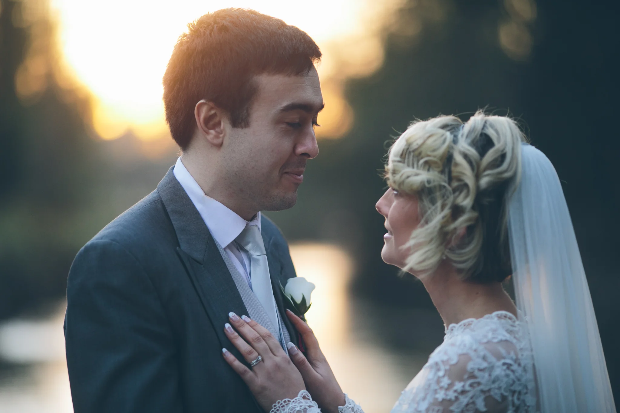 A couple on their wedding day, standing close with their foreheads almost touching, outdoors during sunset.