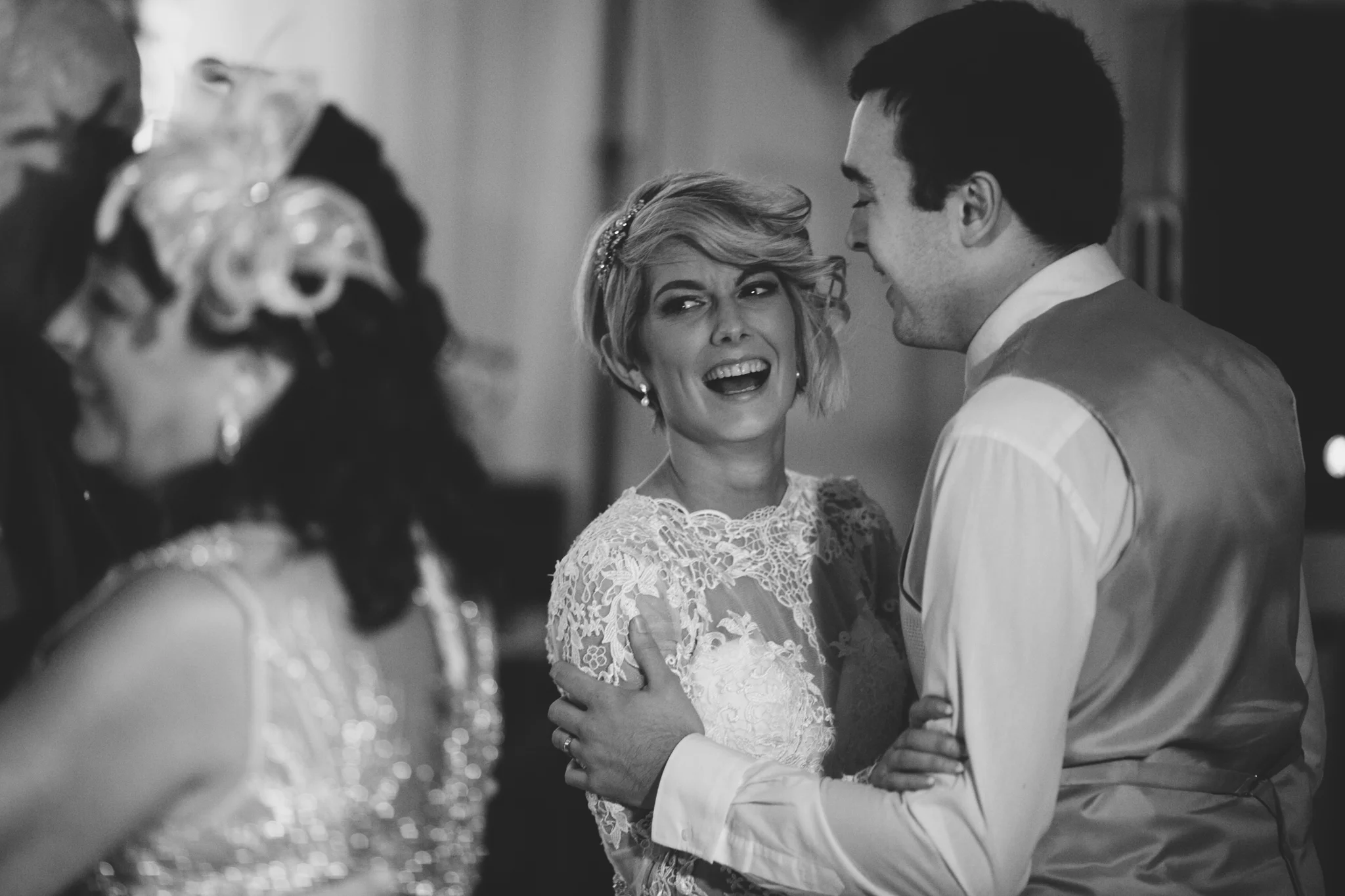 A black and white photo of a woman and a man dancing closely, with the woman smiling and the woman slightly blurry in the foreground.