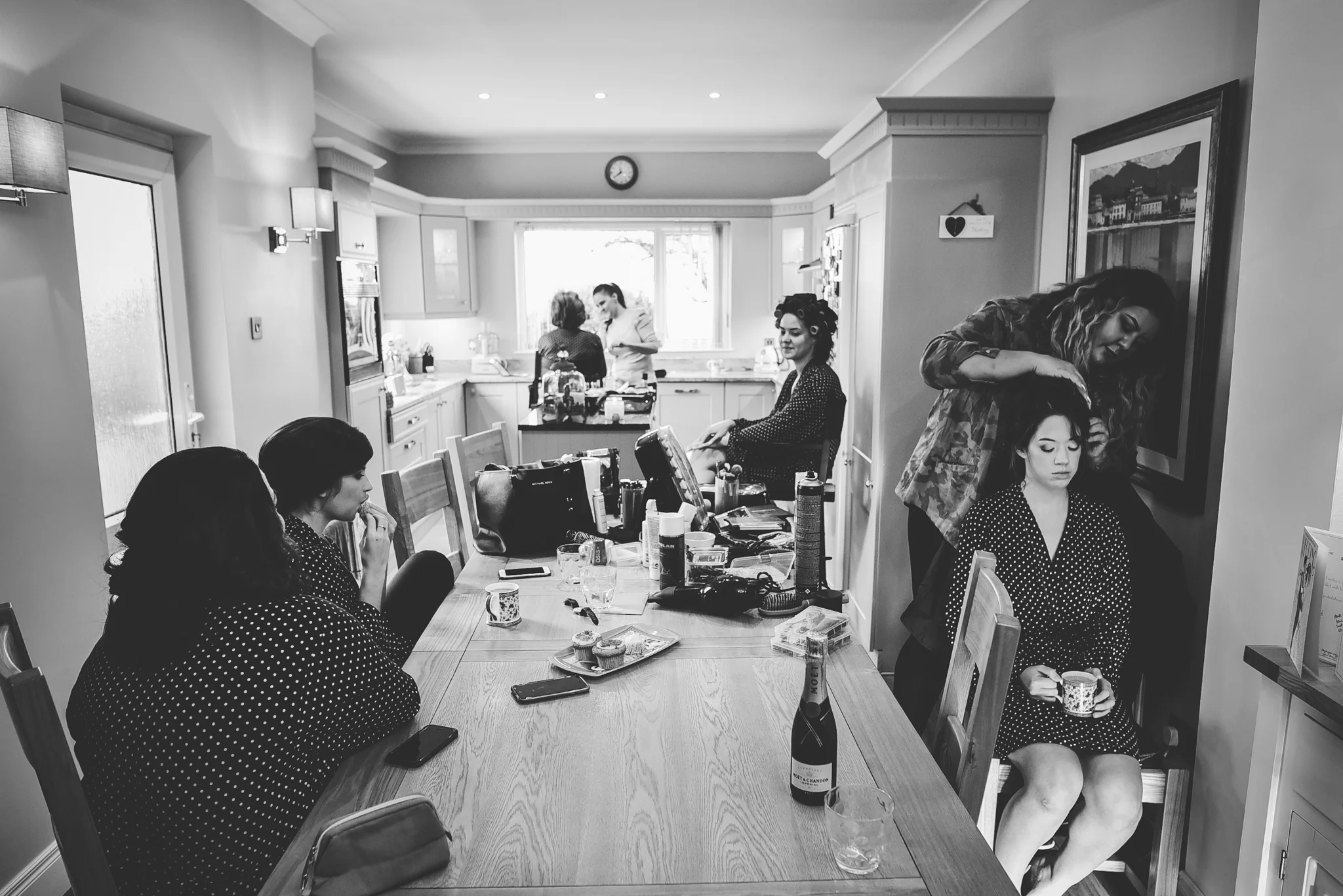 People preparing for a special occasion in a kitchen and dining area, with some sitting and others standing and preparing in the background.