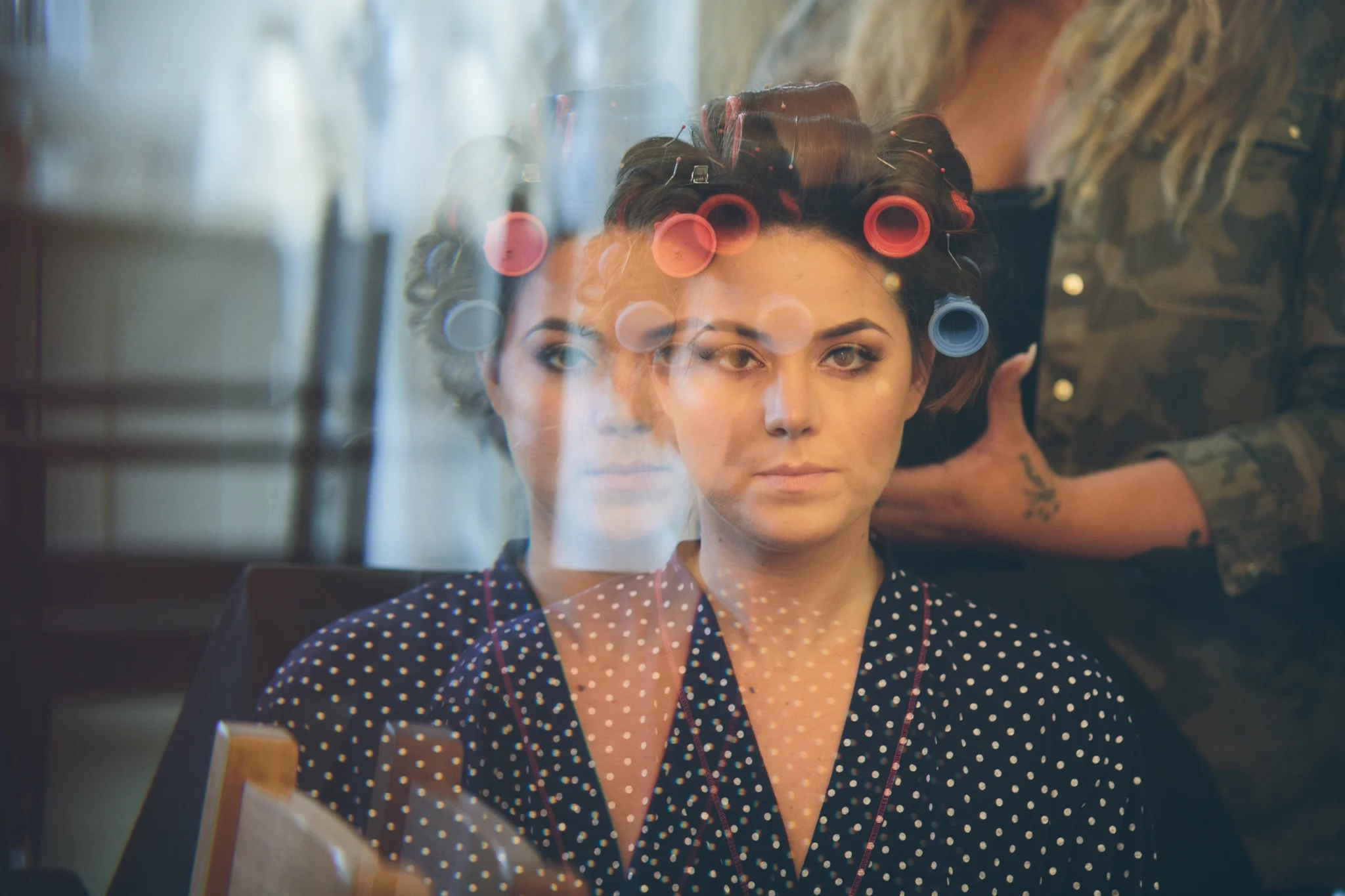 A woman getting her hair styled with curlers in a salon, reflected in a mirror.