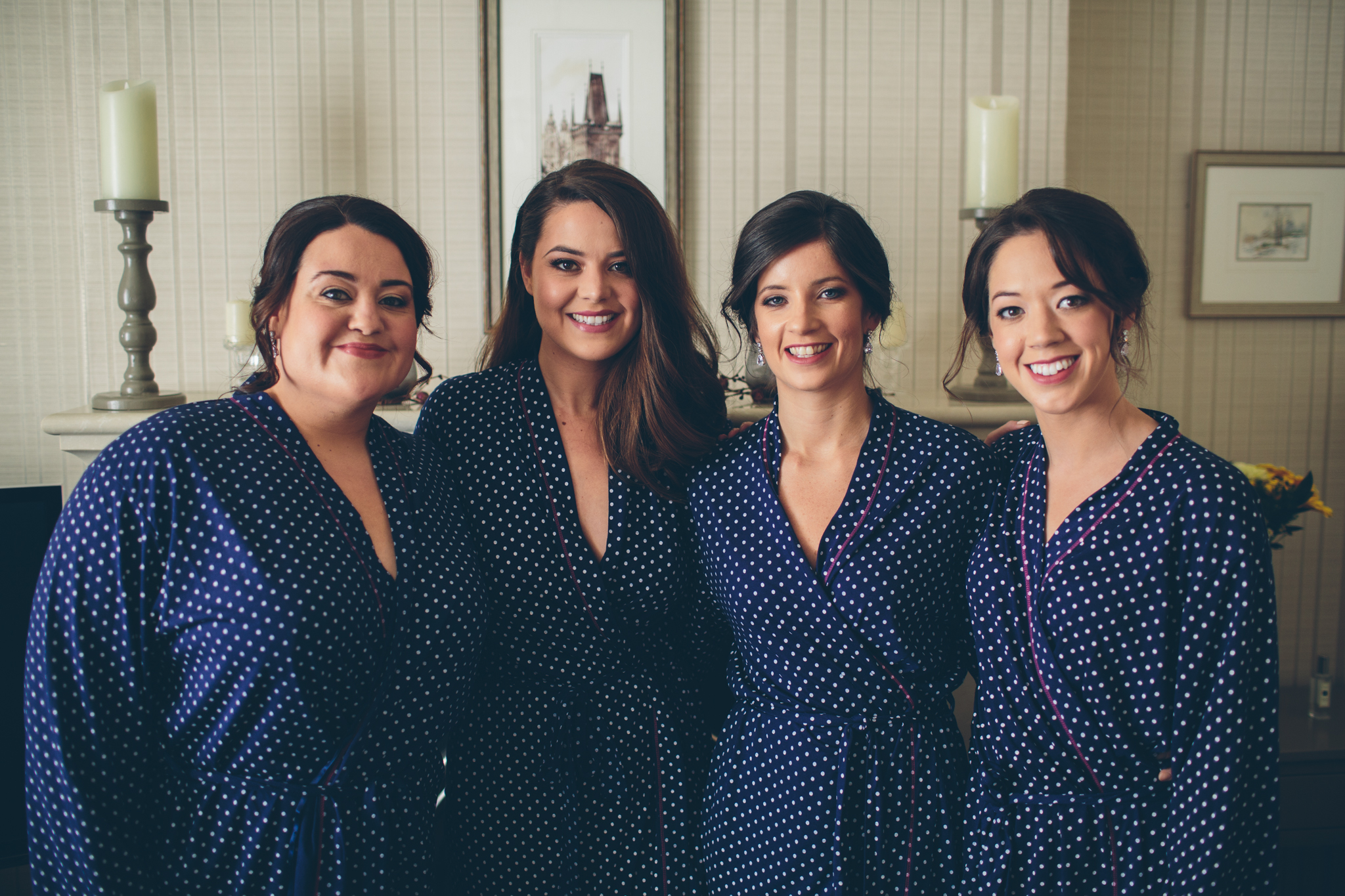 Four women in matching navy blue polka dot pajamas smiling together indoors.