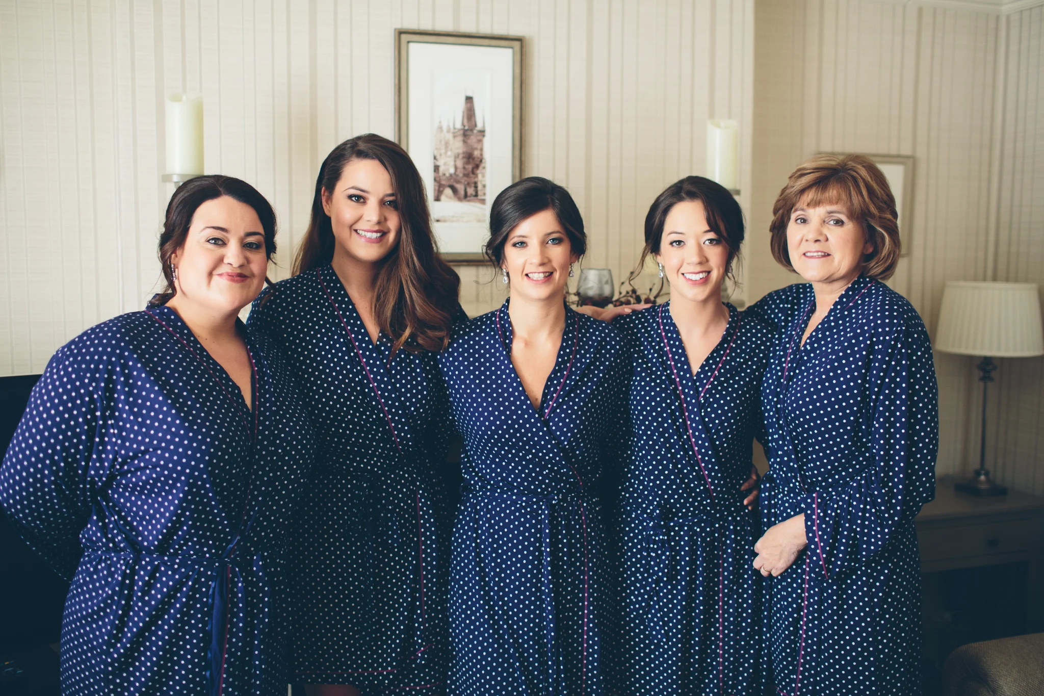 Five women in matching navy blue polka dot pajamas posing together in a living room, smiling at the camera.