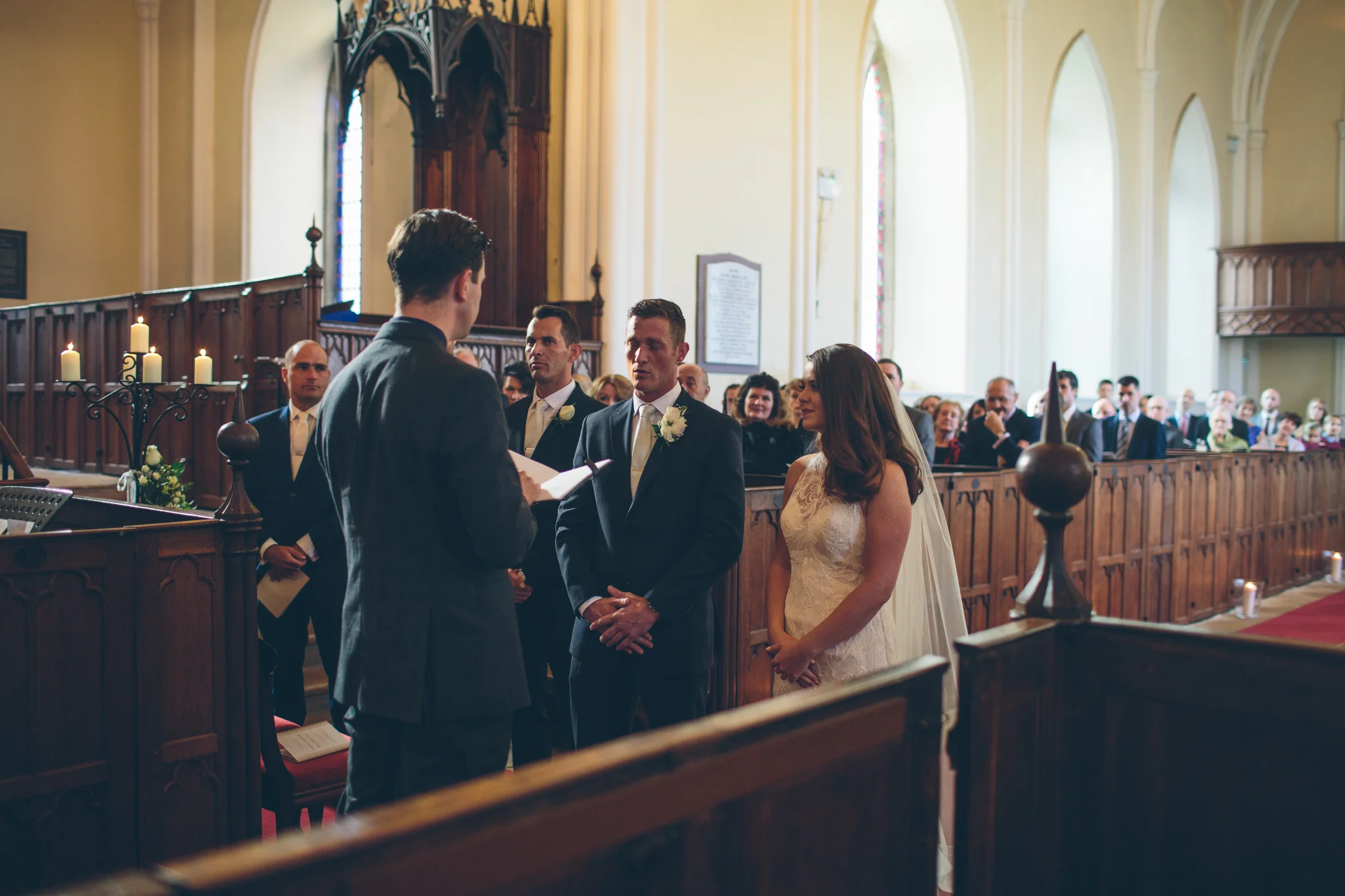 A wedding ceremony inside a church with a priest, bride, groom, and witnesses.