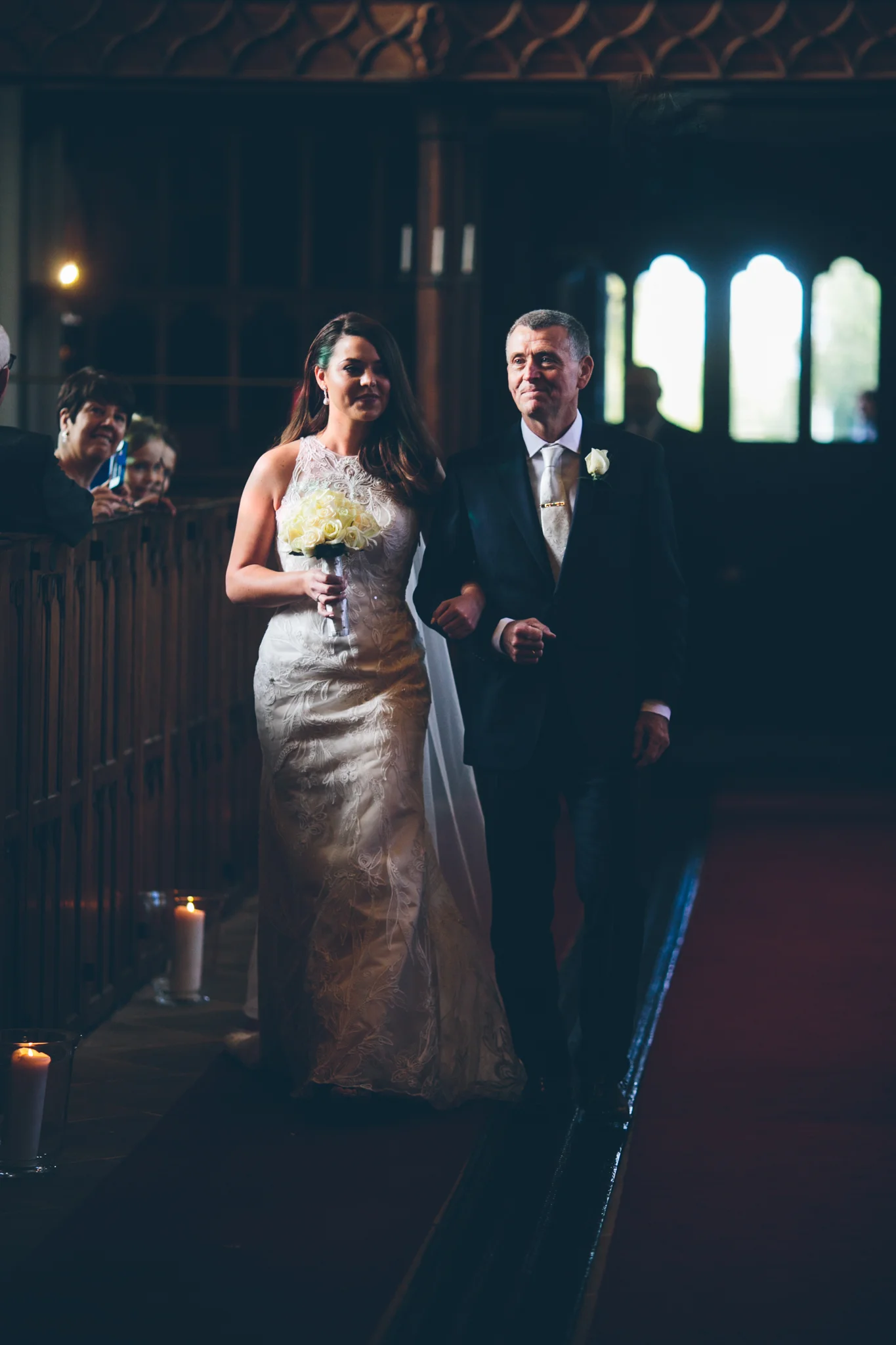 A bride walking down the aisle with an older man, possibly her father, during a wedding ceremony inside a church or chapel.